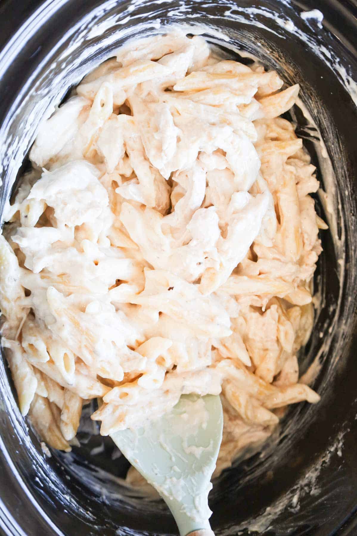 creamy chicken pasta being stirred in a crock pot