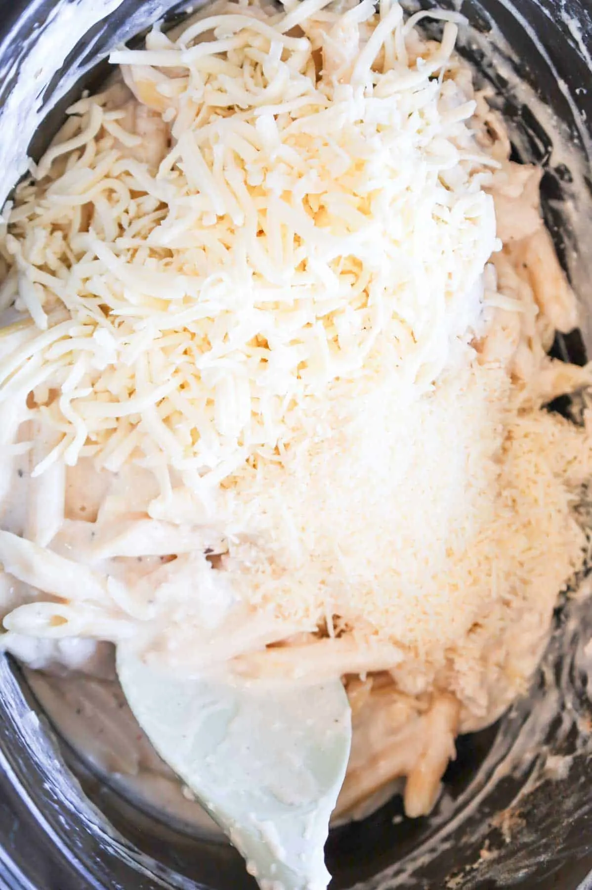 shredded mozzarella and parmesan cheese on top of creamy chicken pasta in a crock pot