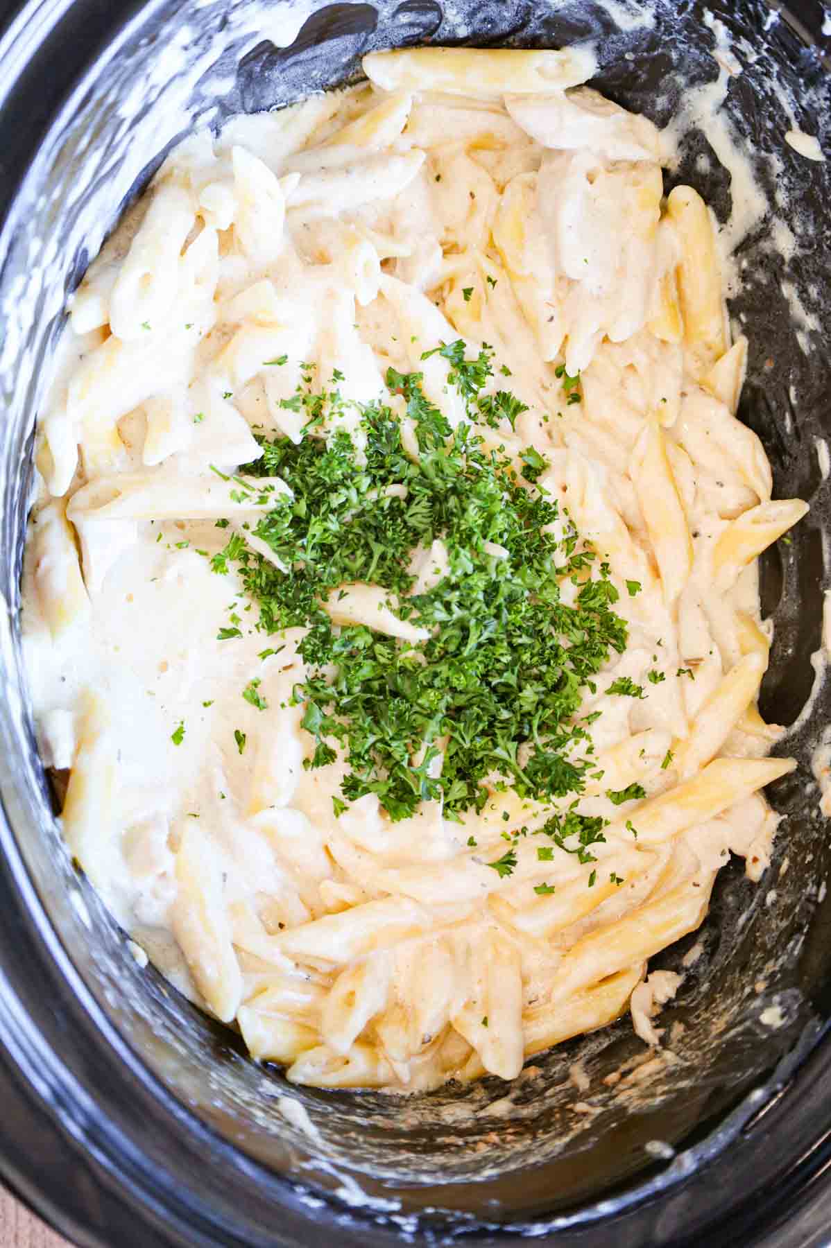 chopped parsley on top of creamy chicken pasta in a crock pot