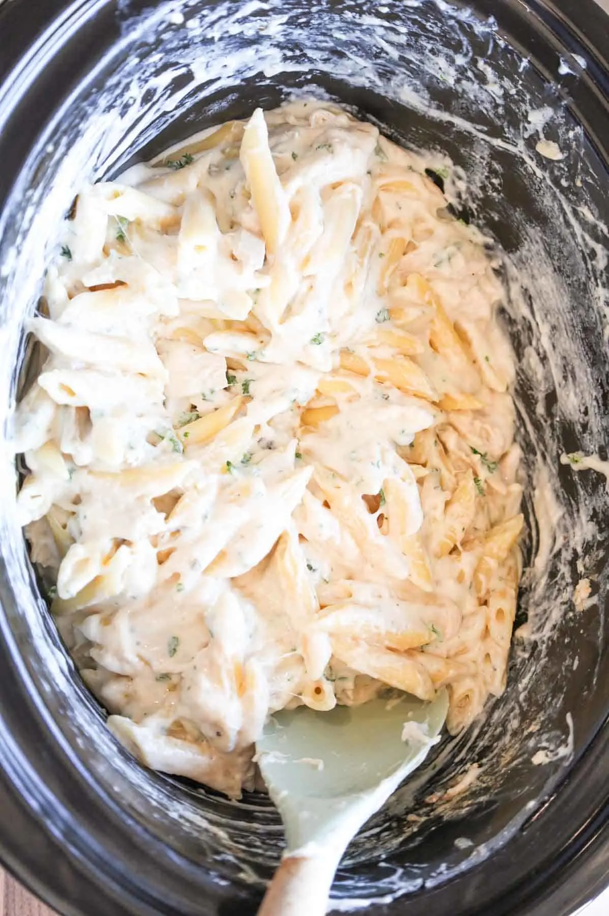 chopped parsley being stirred into creamy chicken pasta in a crock pot