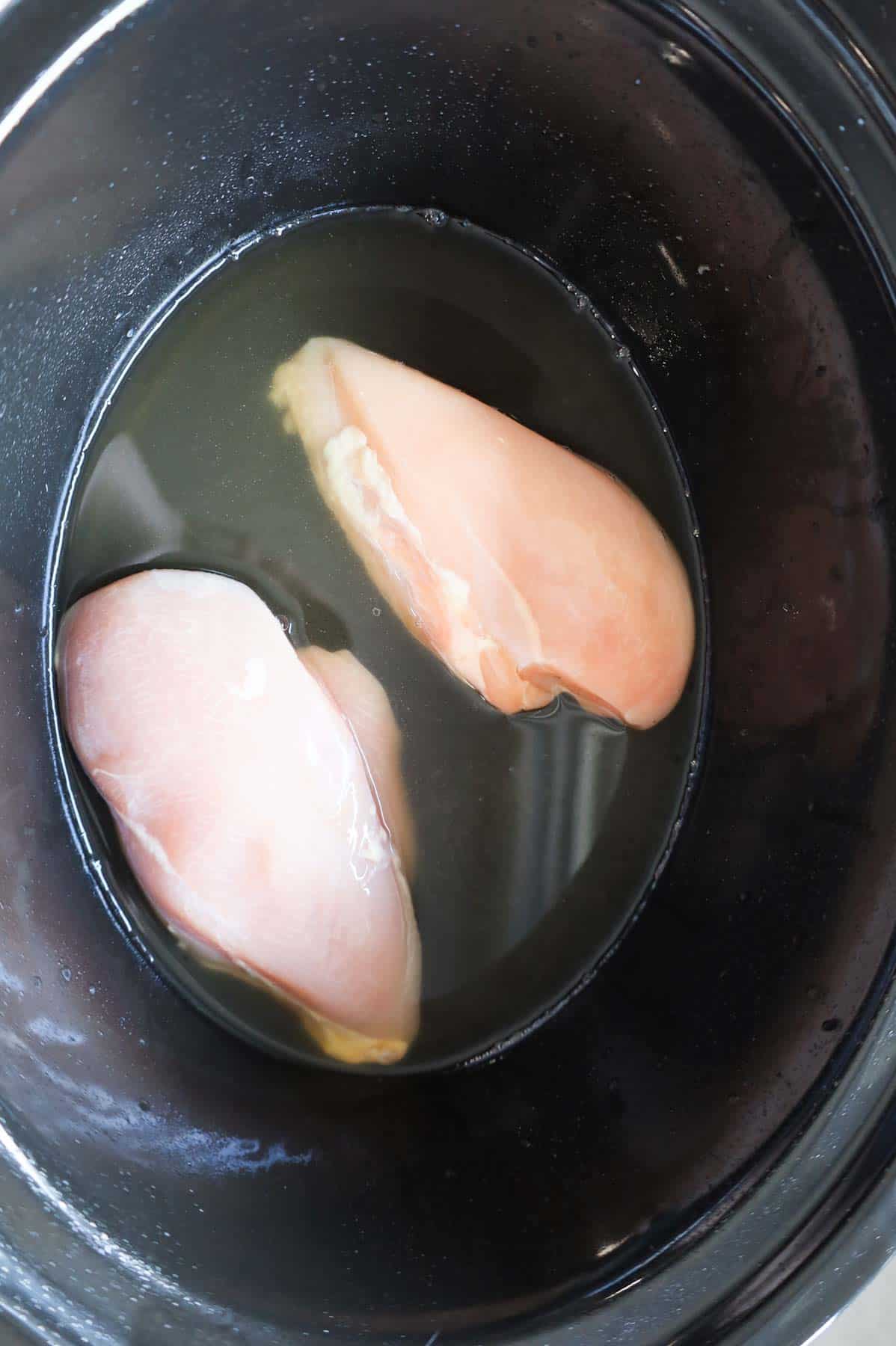 raw boneless, skinless chicken breasts in a Crock Pot with chicken broth