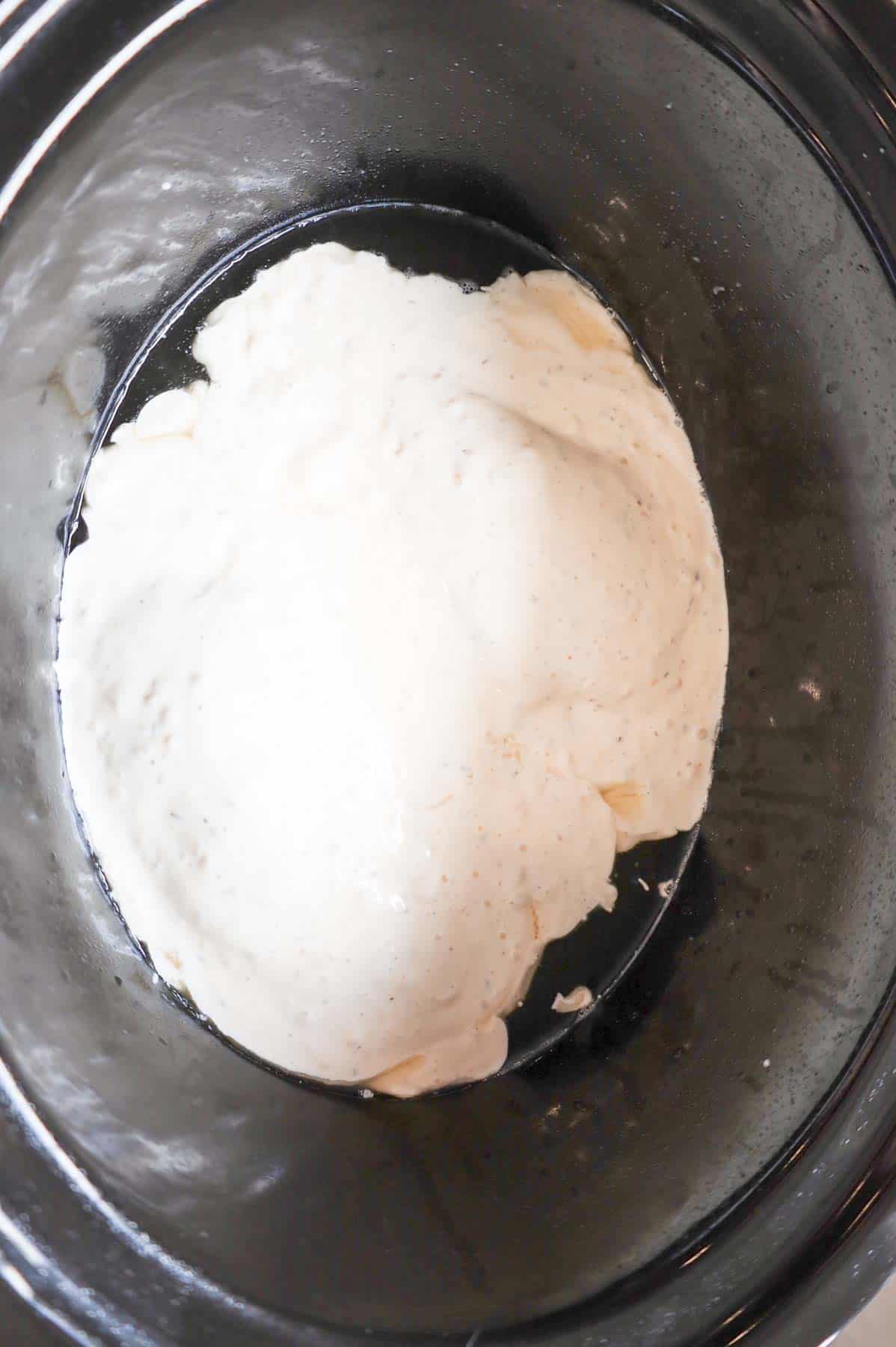 garlic parmesan wing sauce poured over chicken breasts in a crock pot