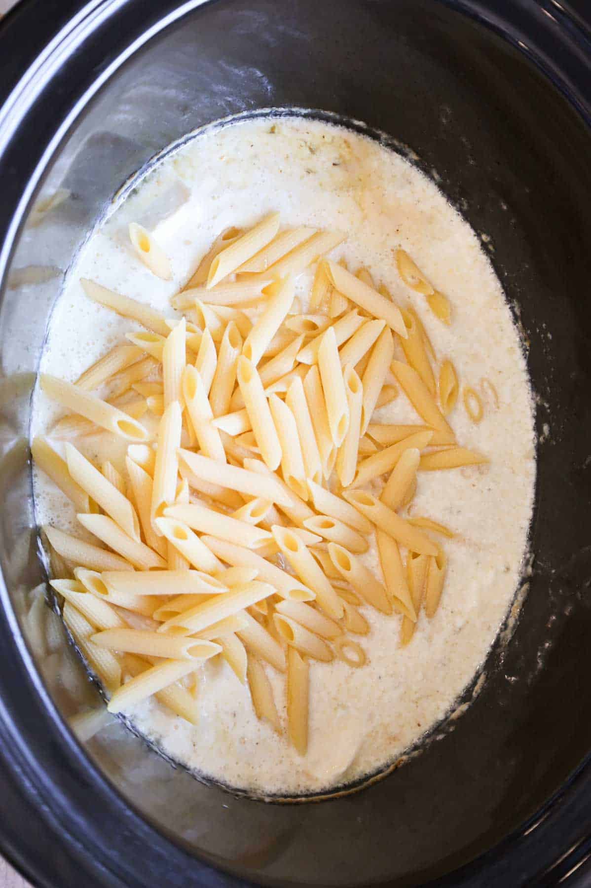 uncooked penne noodles added to crock pot with garlic parmesan sauce