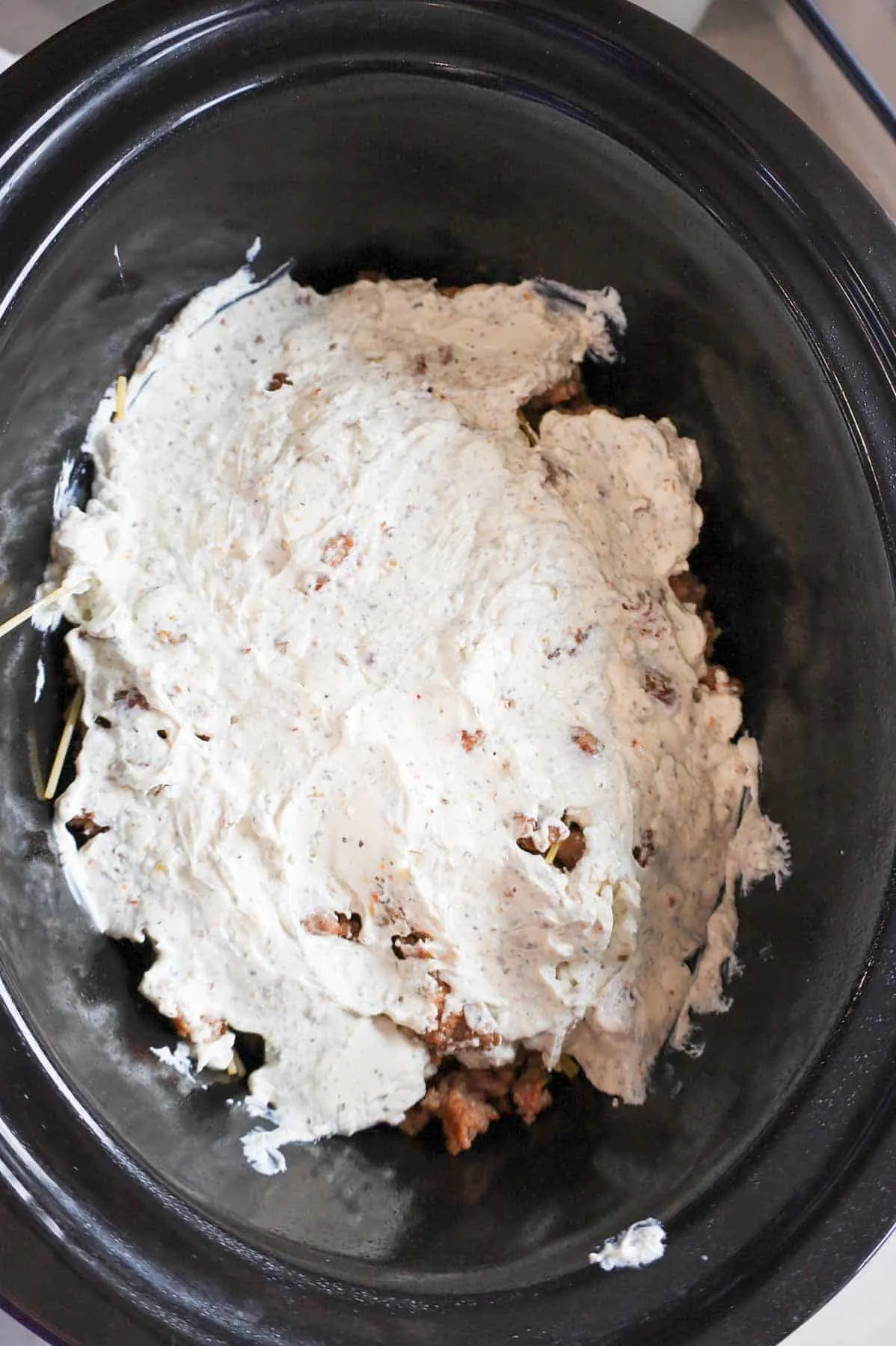 sour cream and cream cheese mixture spread over crumbled sausage and spaghetti in a crock pot