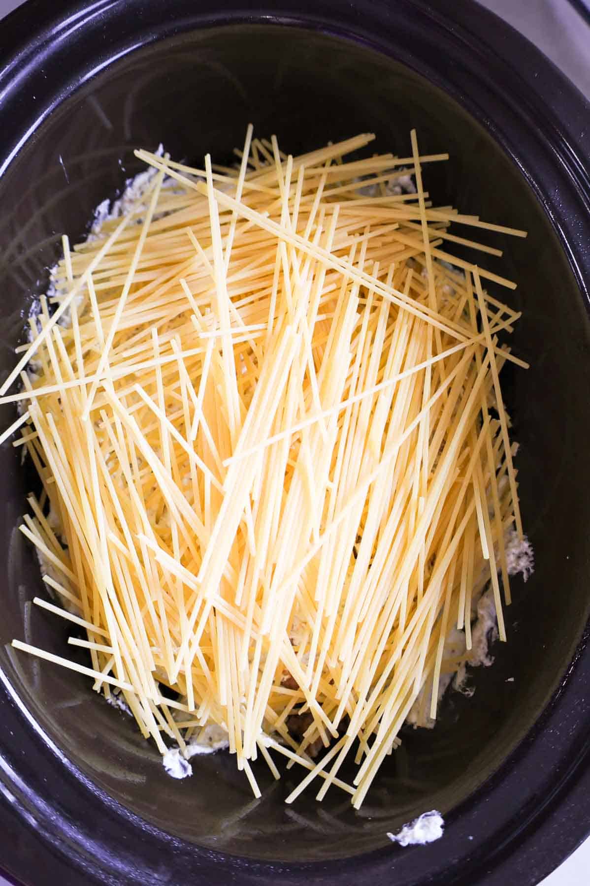 uncooked spaghetti noodles on top of cream cheese mixture in a crock pot