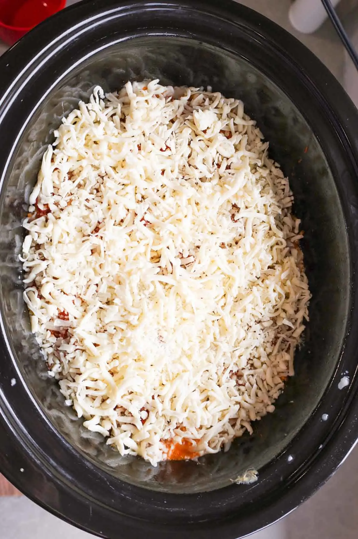 shredded mozzarella cheese on top of spaghetti in a crock pot