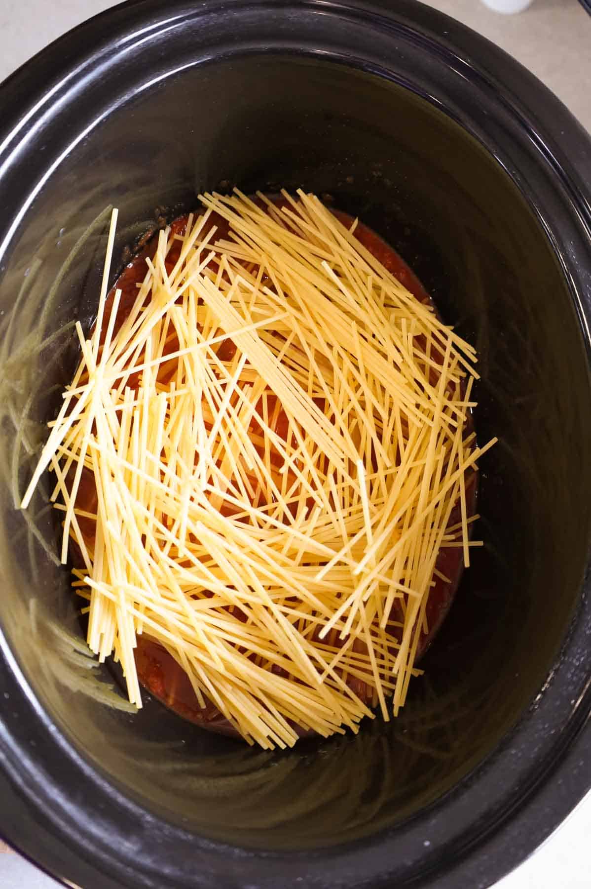 uncooked spaghetti noodles on top of marinara sauce in a crock pot