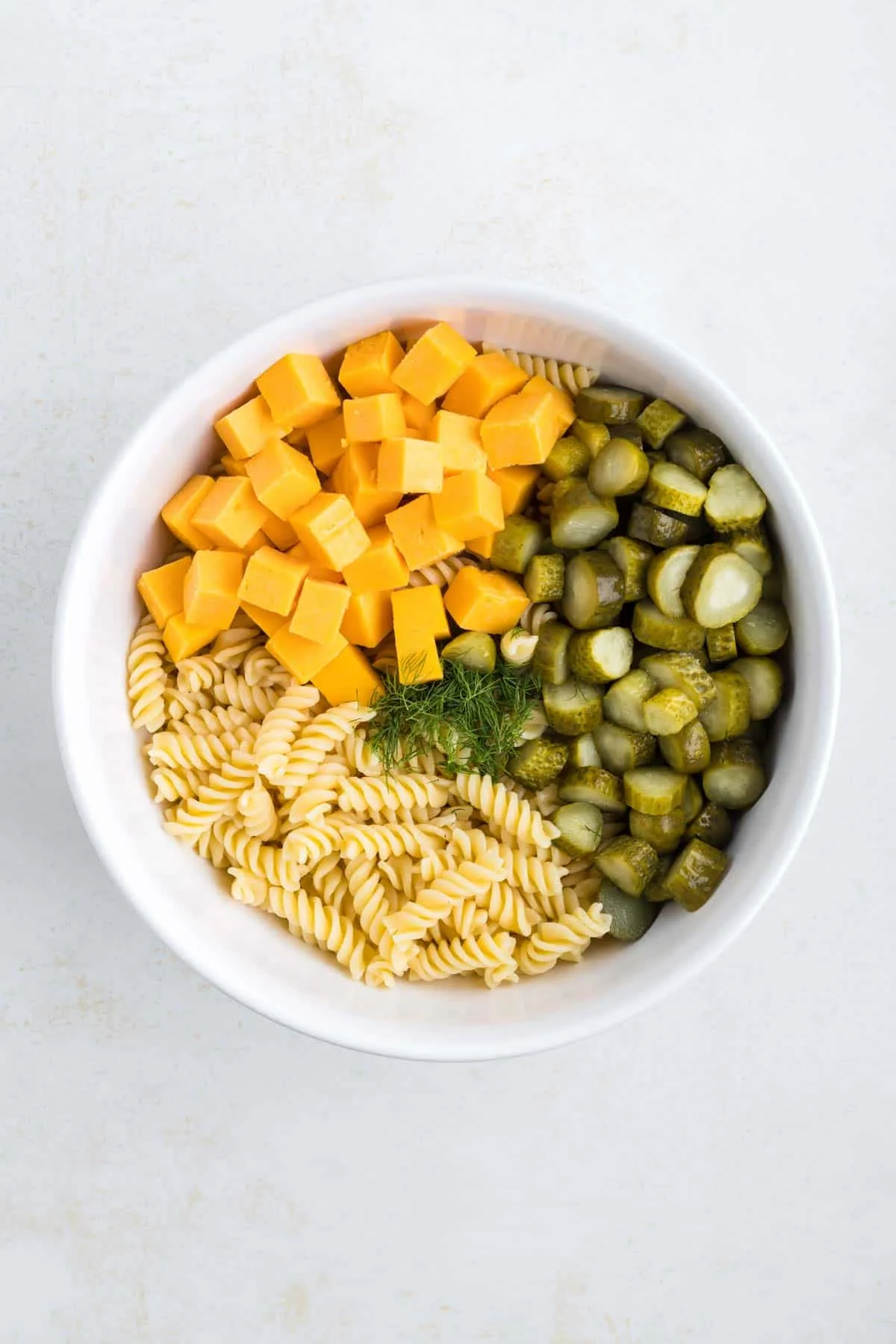 cheddar cheese cubes, sliced pickles, chopped fresh dill and cooked rotini noodles in a large mixing bowl