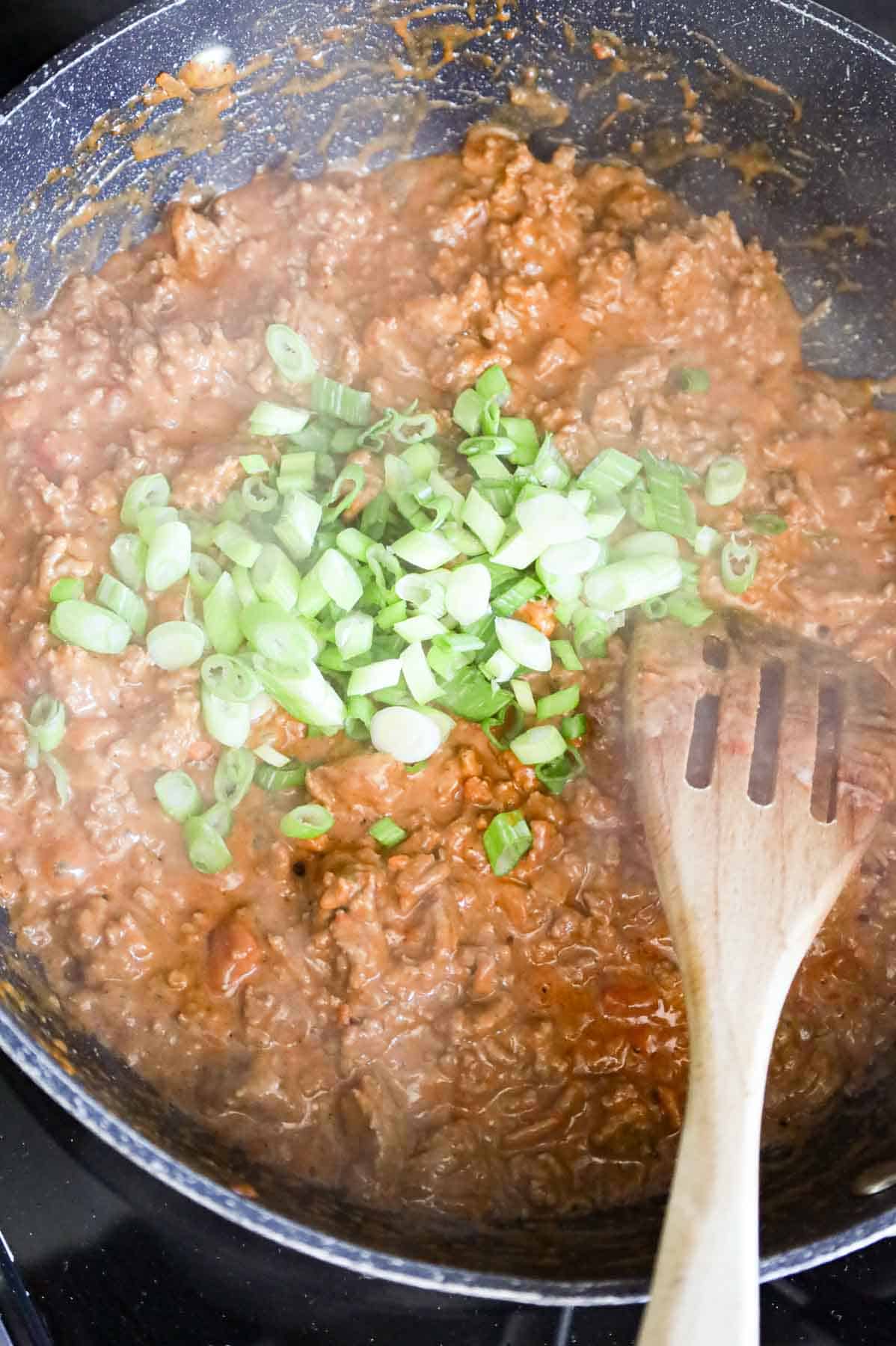 chopped green onions on top of ground beef taco mixture in a skillet