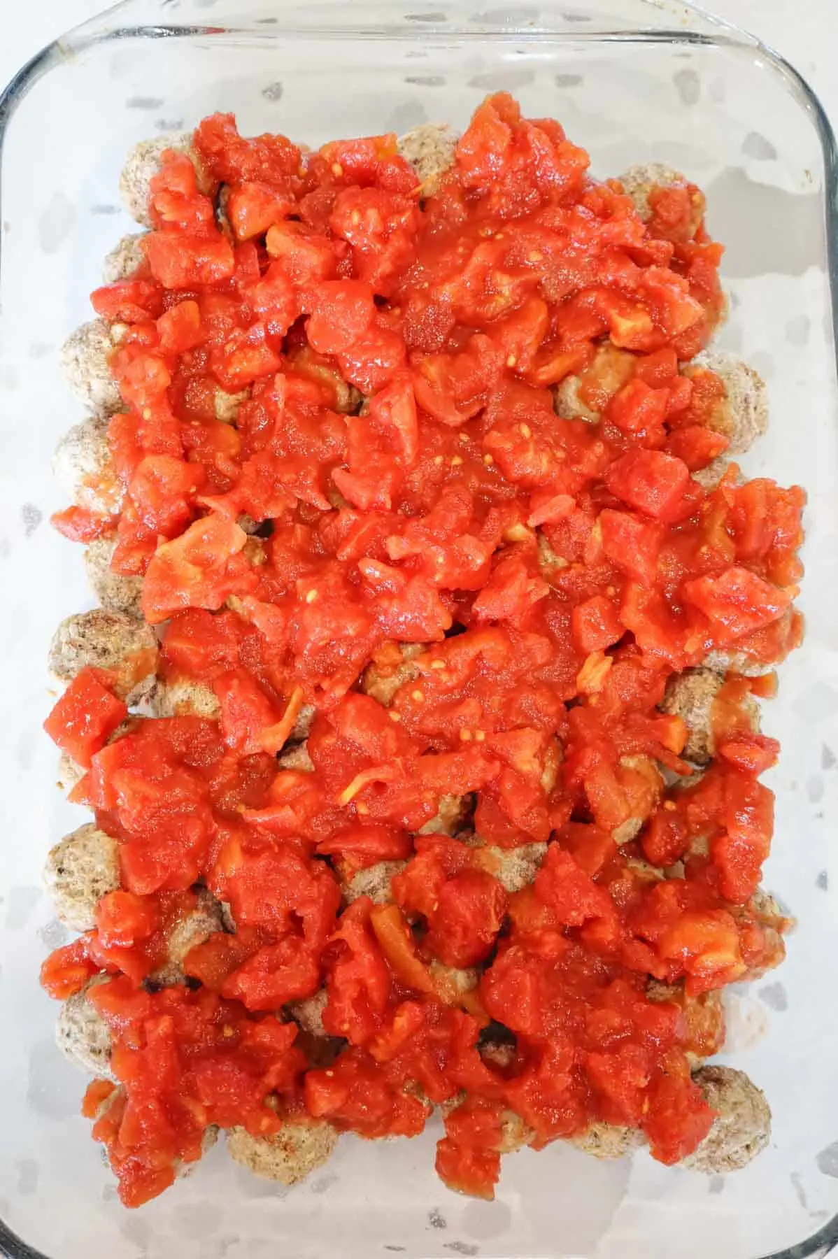 diced tomatoes on top of meatballs in a baking dish
