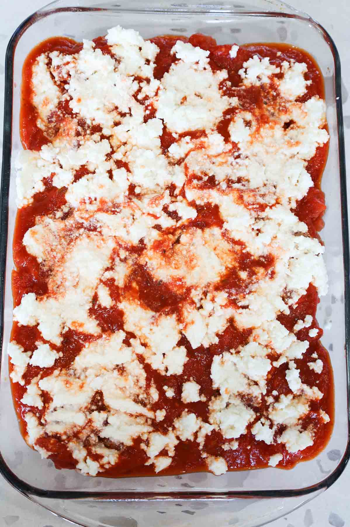 ricotta and marinara on top of meatballs in a baking dish