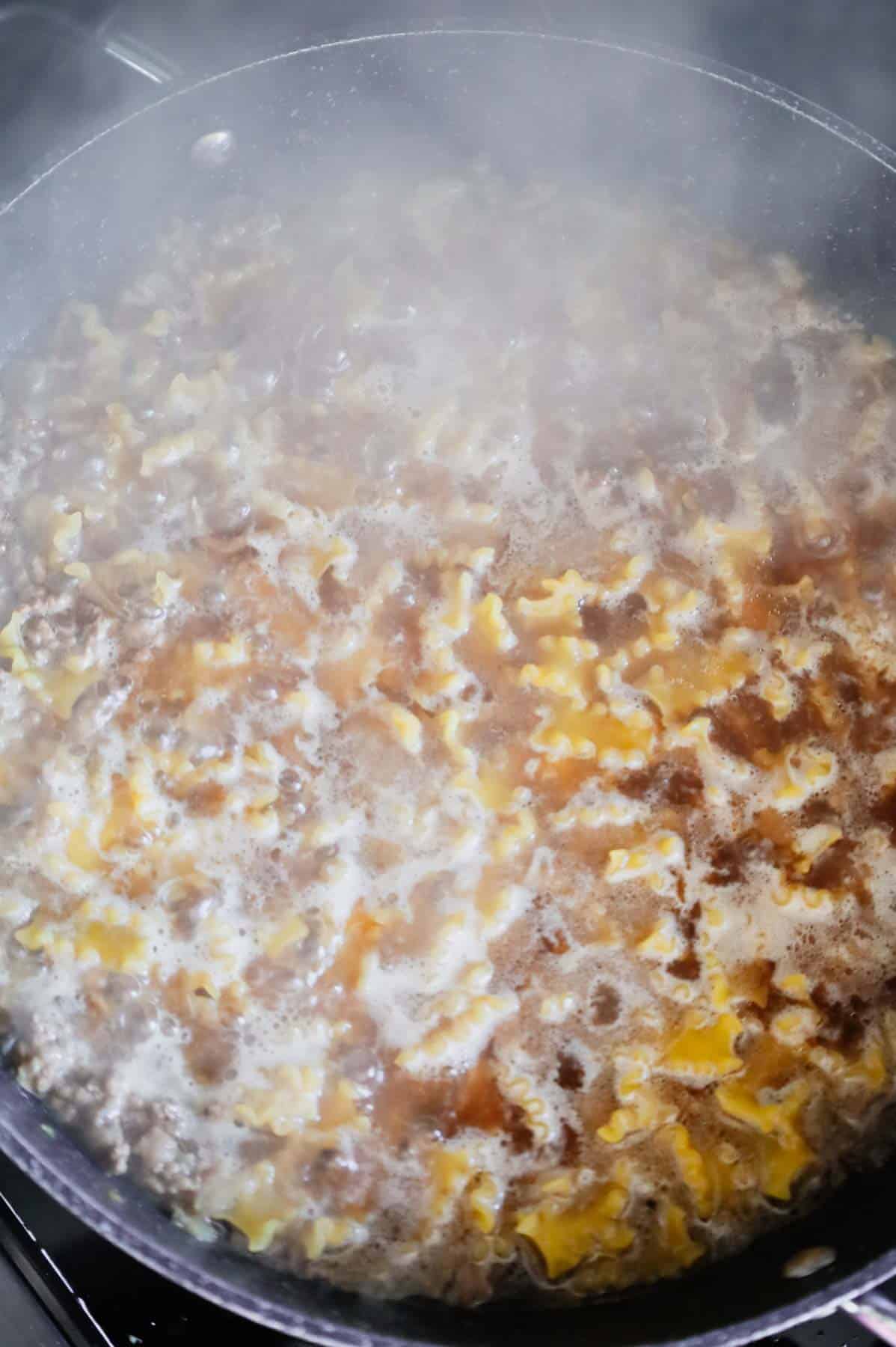 pasta cooking in a beef broth in a skillet