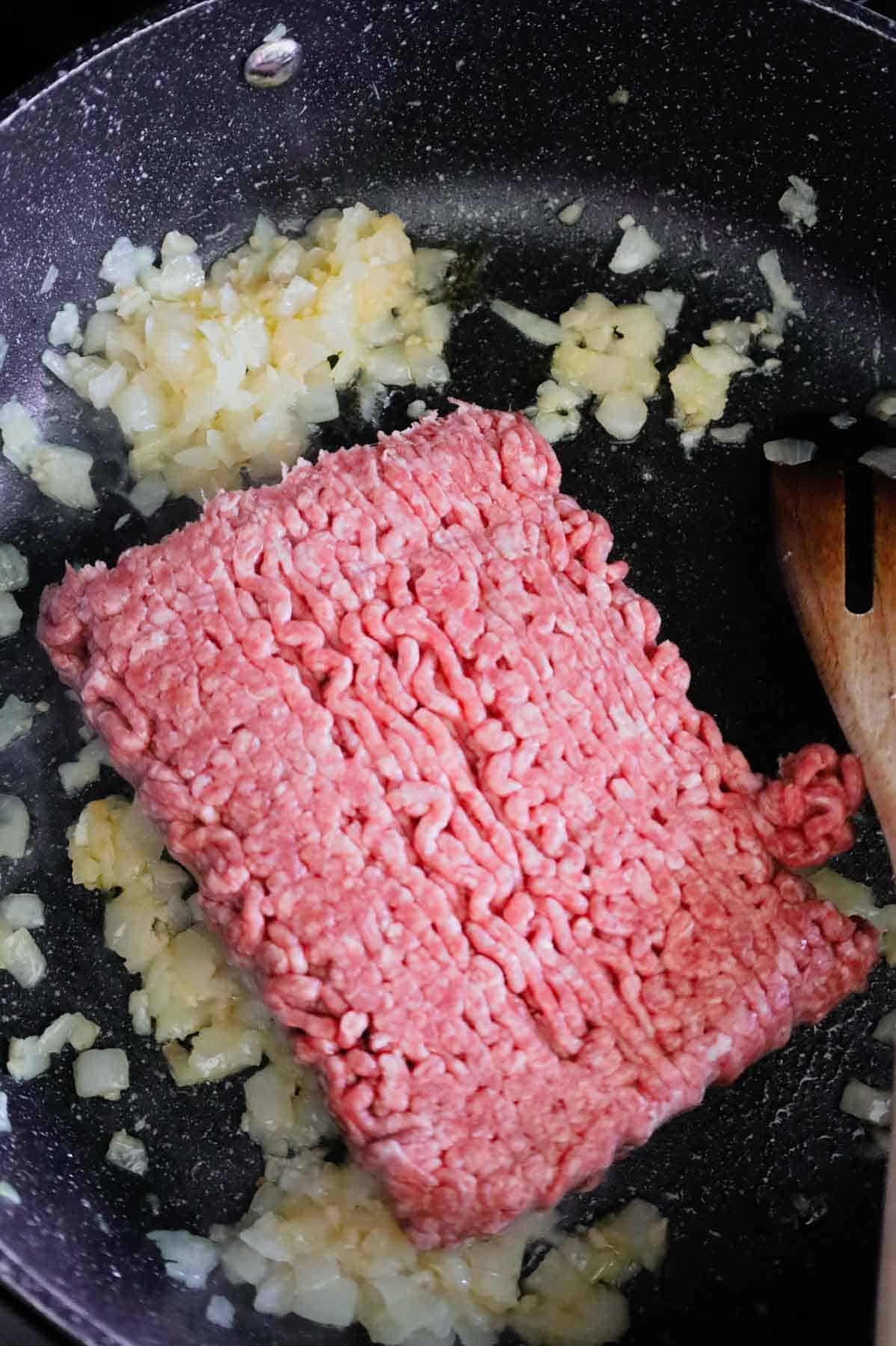 ground beef added to a skillet with diced onions and minced garlic