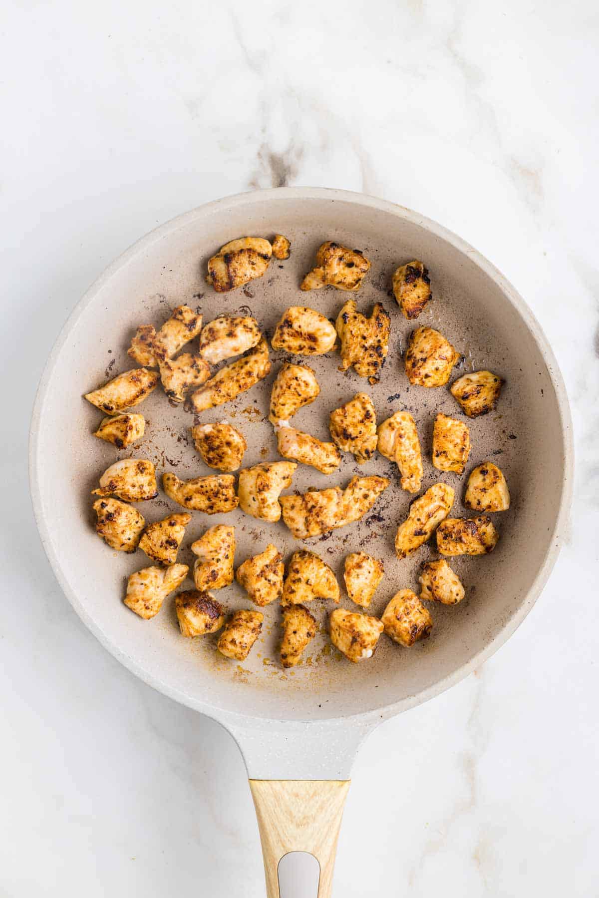 Cajun seasoned chicken breast chunks cooking in a skillet