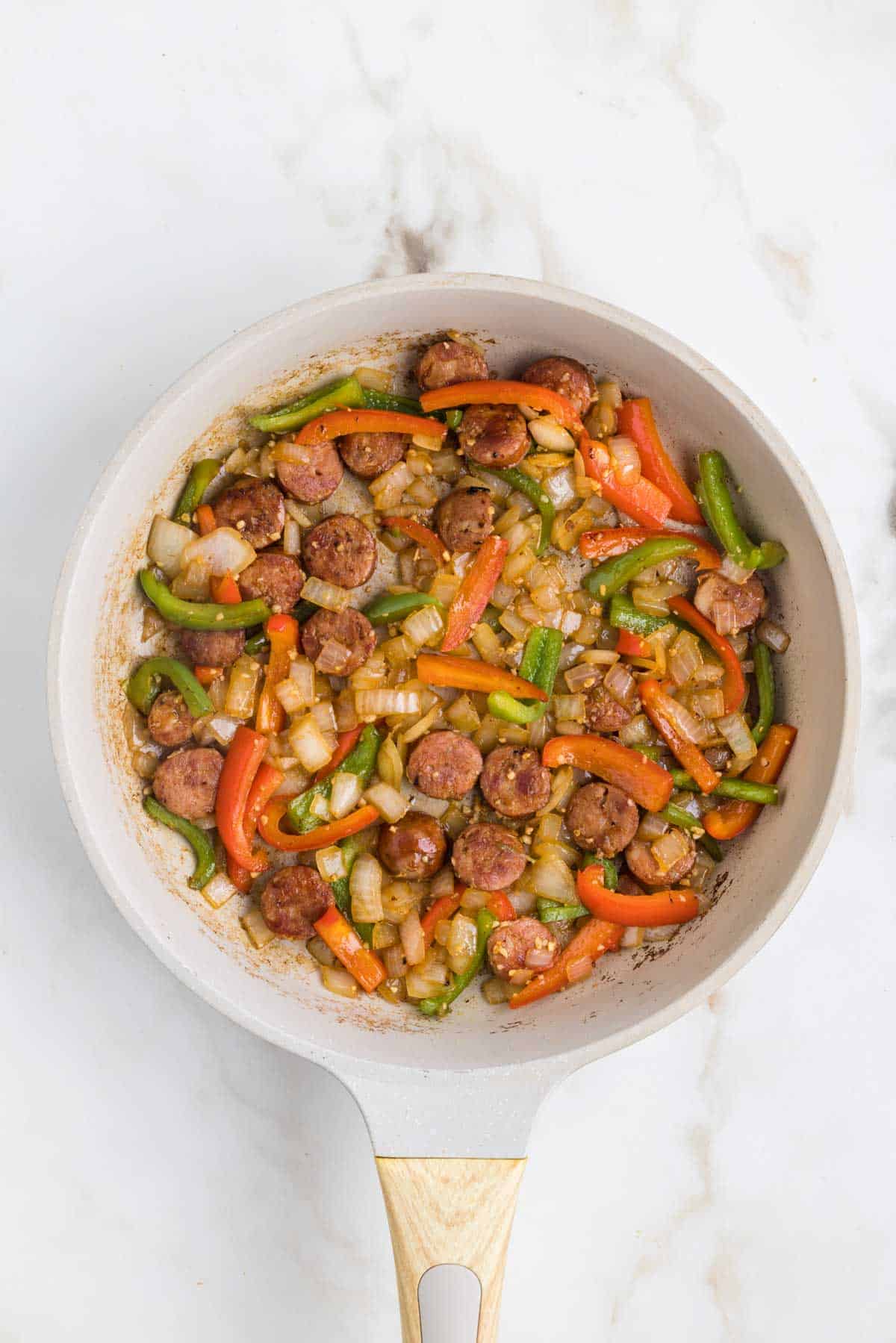 sliced bell peppers, onions and sausage cooking in a skillet