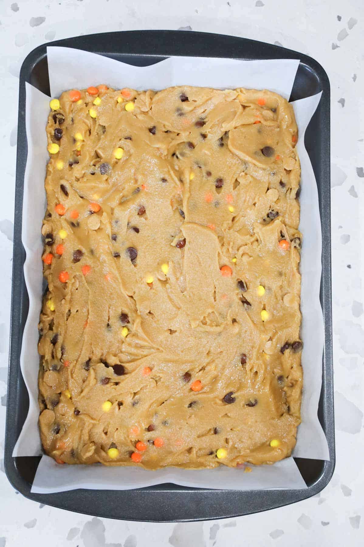 peanut butter blondie batter in a parchment lined baking pan