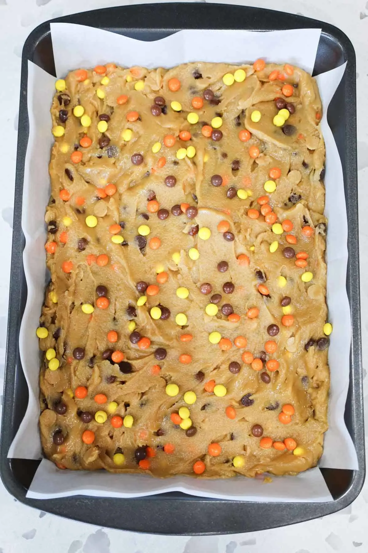 mini Reese's pieces candies on top of peanut butter blondie batter in a baking pan