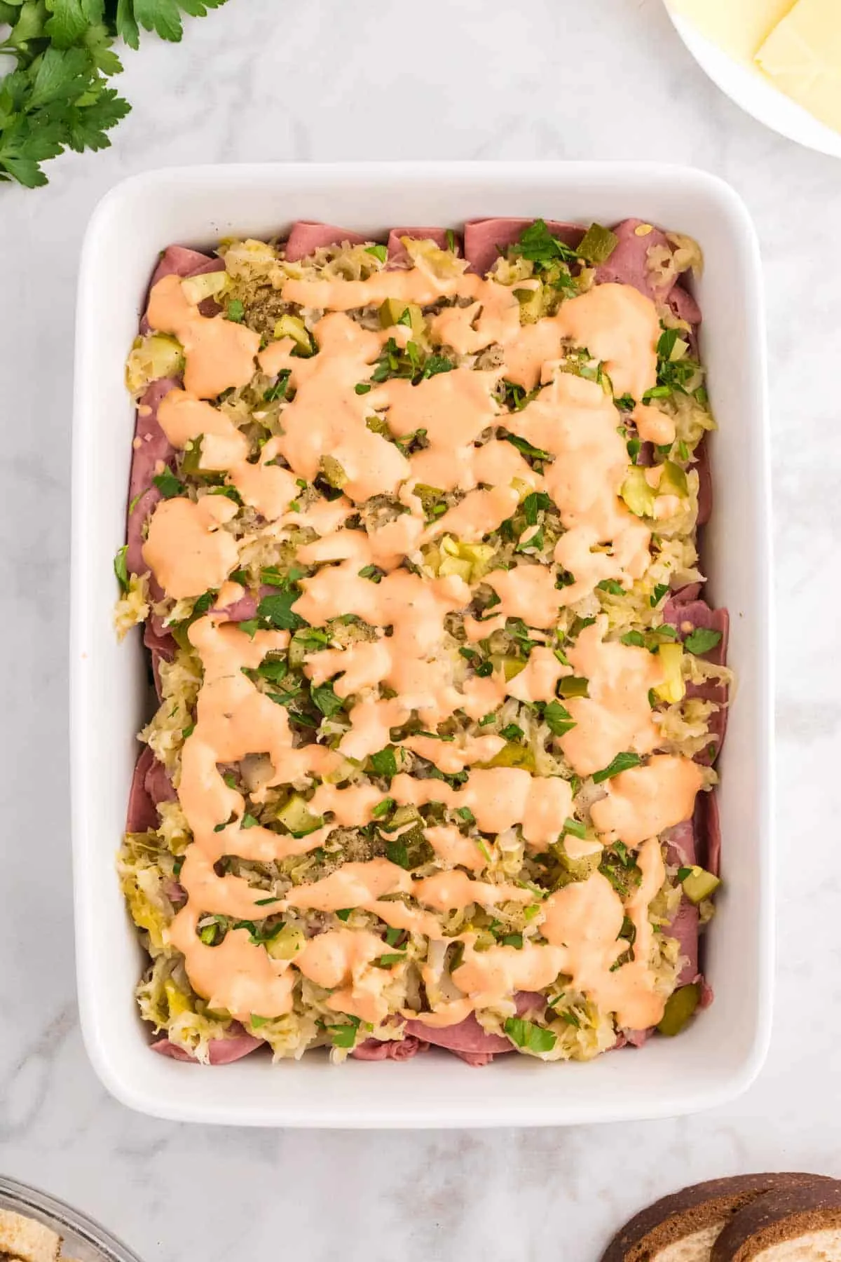 Thousand Island dressing on top of chopped pickles, sauerkraut and corned beef in a casserole dish