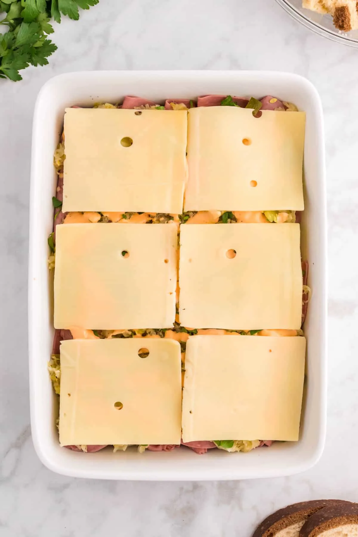 Swiss cheese slices on top of sauerkraut and corned beef in a casserole dish