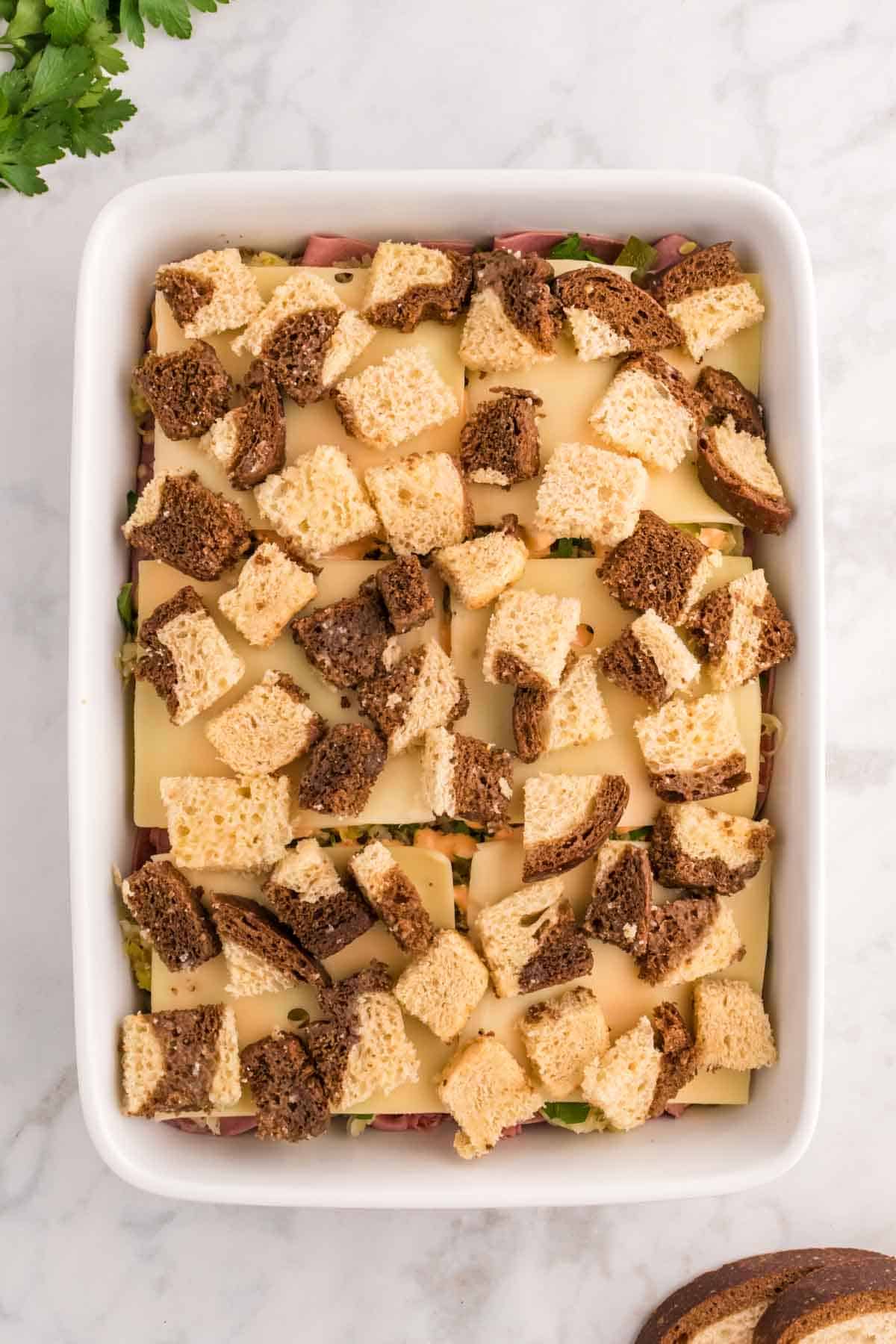 cubes of marble rye bread on top of Swiss cheese in a casserole dish