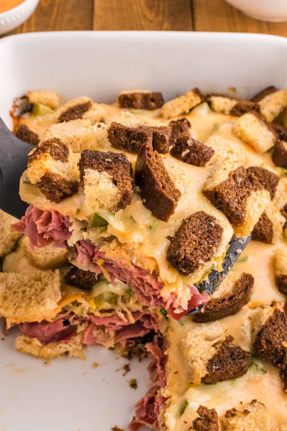 Reuben Casserole is a tasty dish loaded with cubes of rye bread, sliced corned beef, sauerkraut, dill pickles, Swiss cheese and Thousand Island dressing.