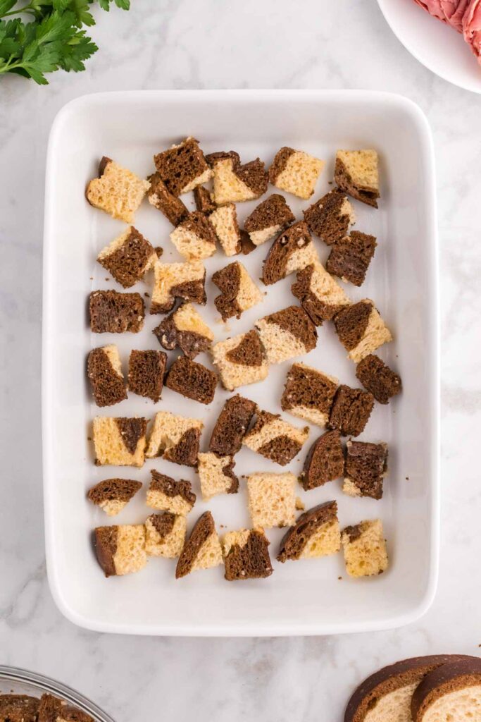 cubes of marble rye bread in the bottom of a a baking dish