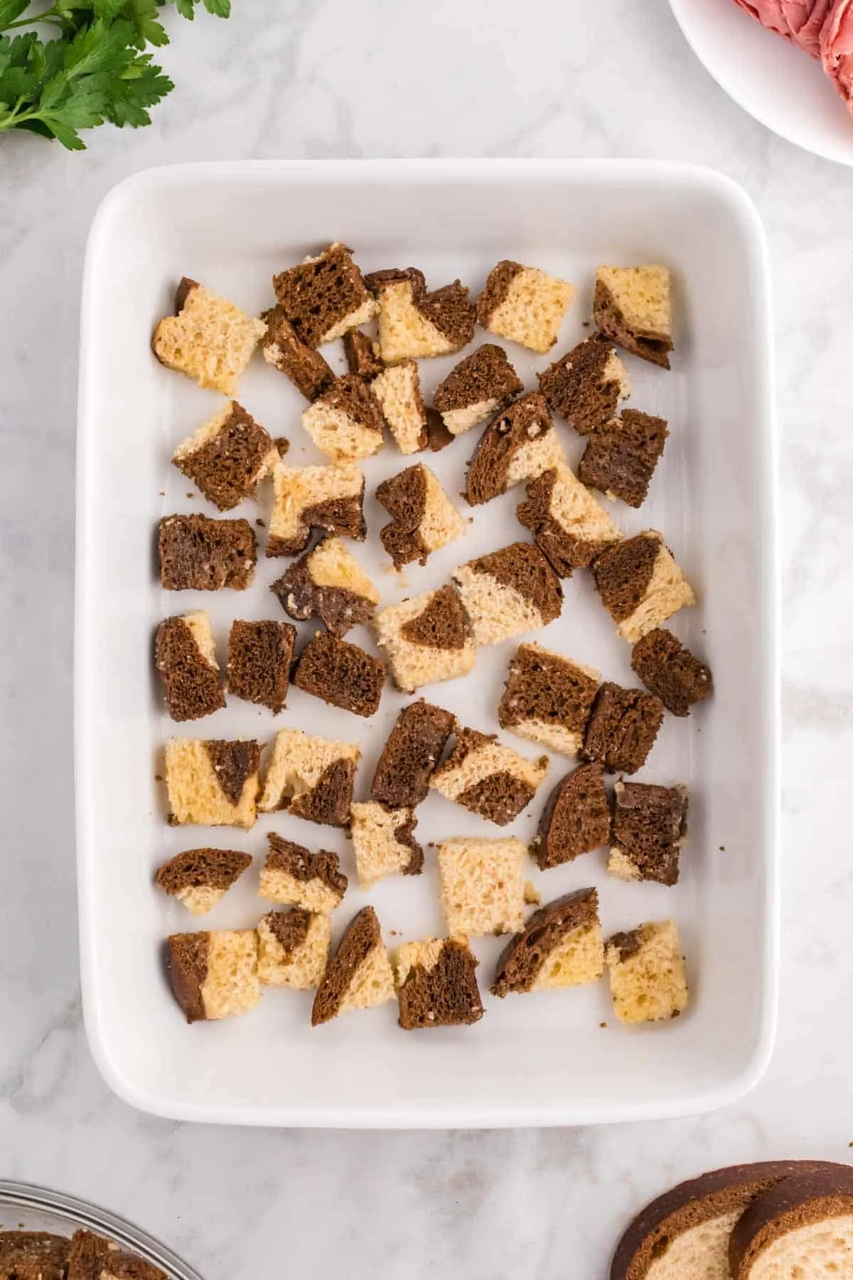 cubes of marble rye bread in the bottom of a a baking dish