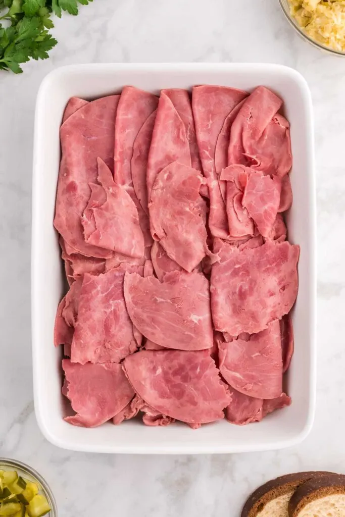 sliced corned beef on top of marble rye in a casserole dish