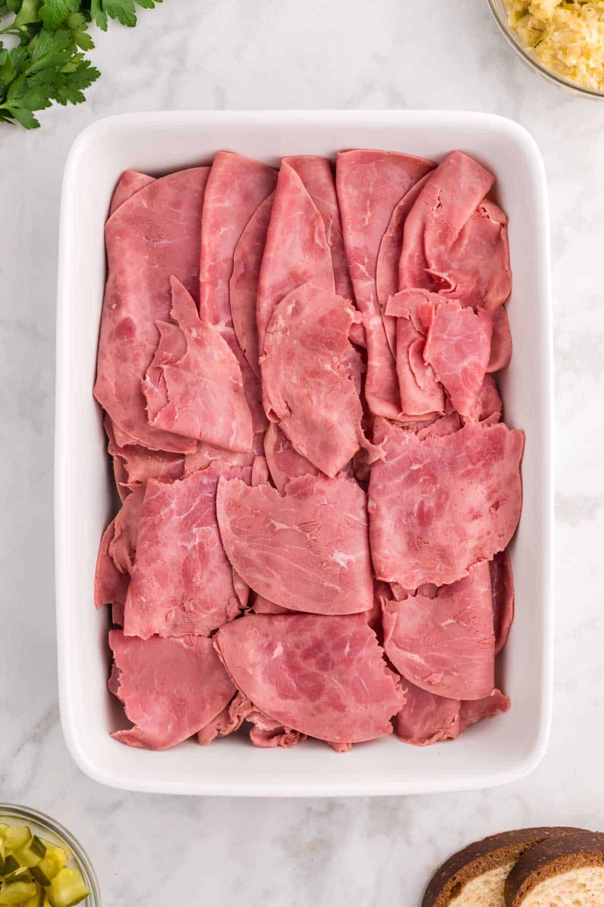 sliced corned beef on top of marble rye in a casserole dish