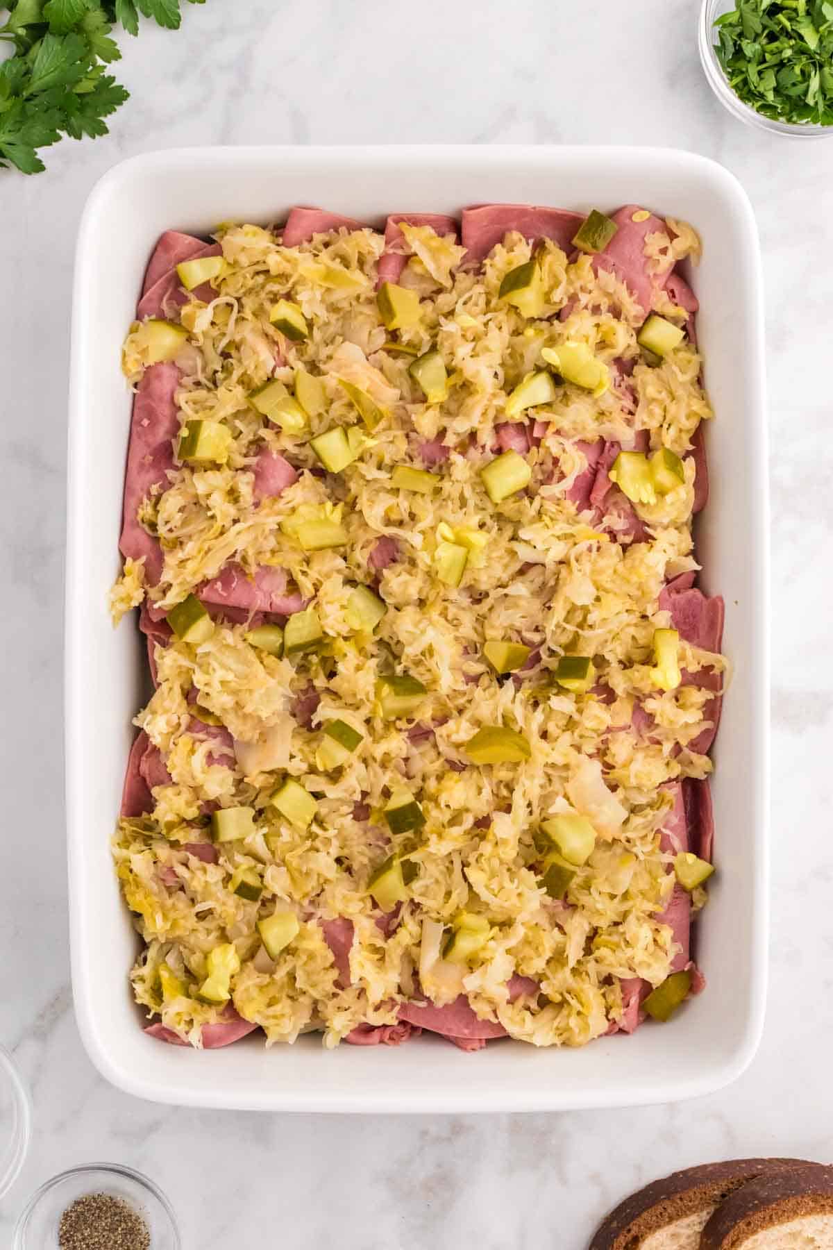 chopped dill pickles and sauerkraut on top of corned beef in a casserole dish