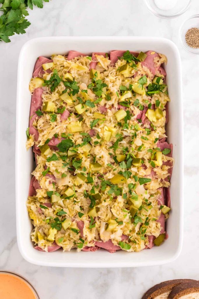 parsley, pickles sauerkraut on top of corned beef in a casserole dish