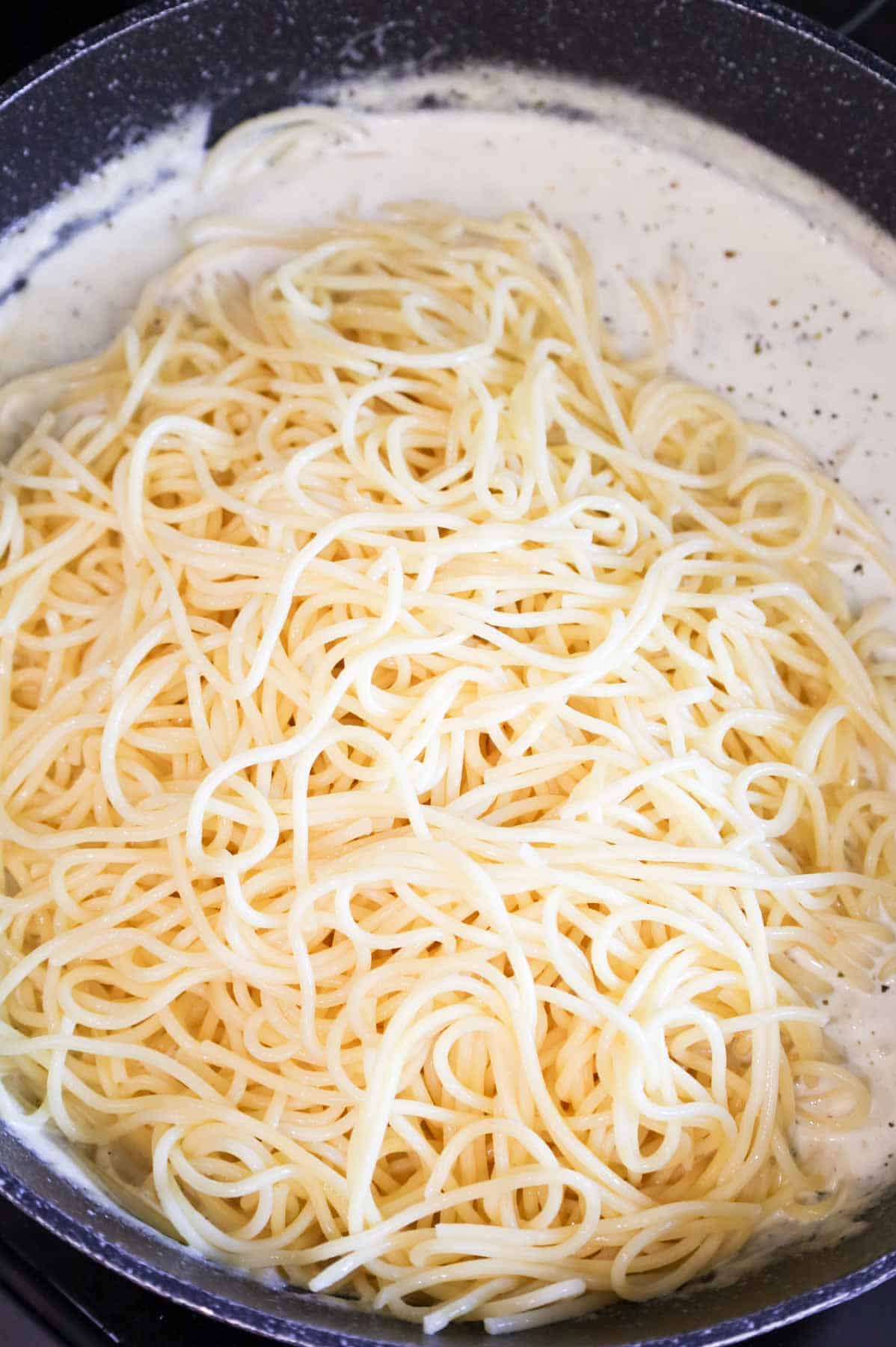 cooked spaghetti added to a skillet with cream sauce