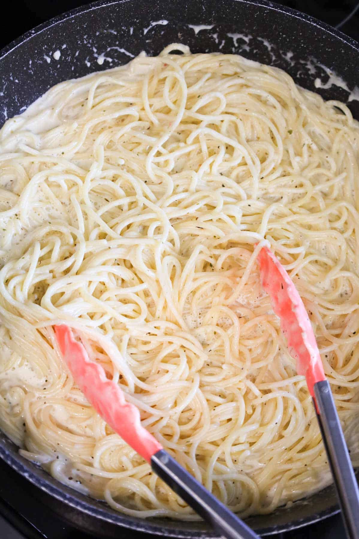 spaghetti being tossed in a cream sauce in a skillet