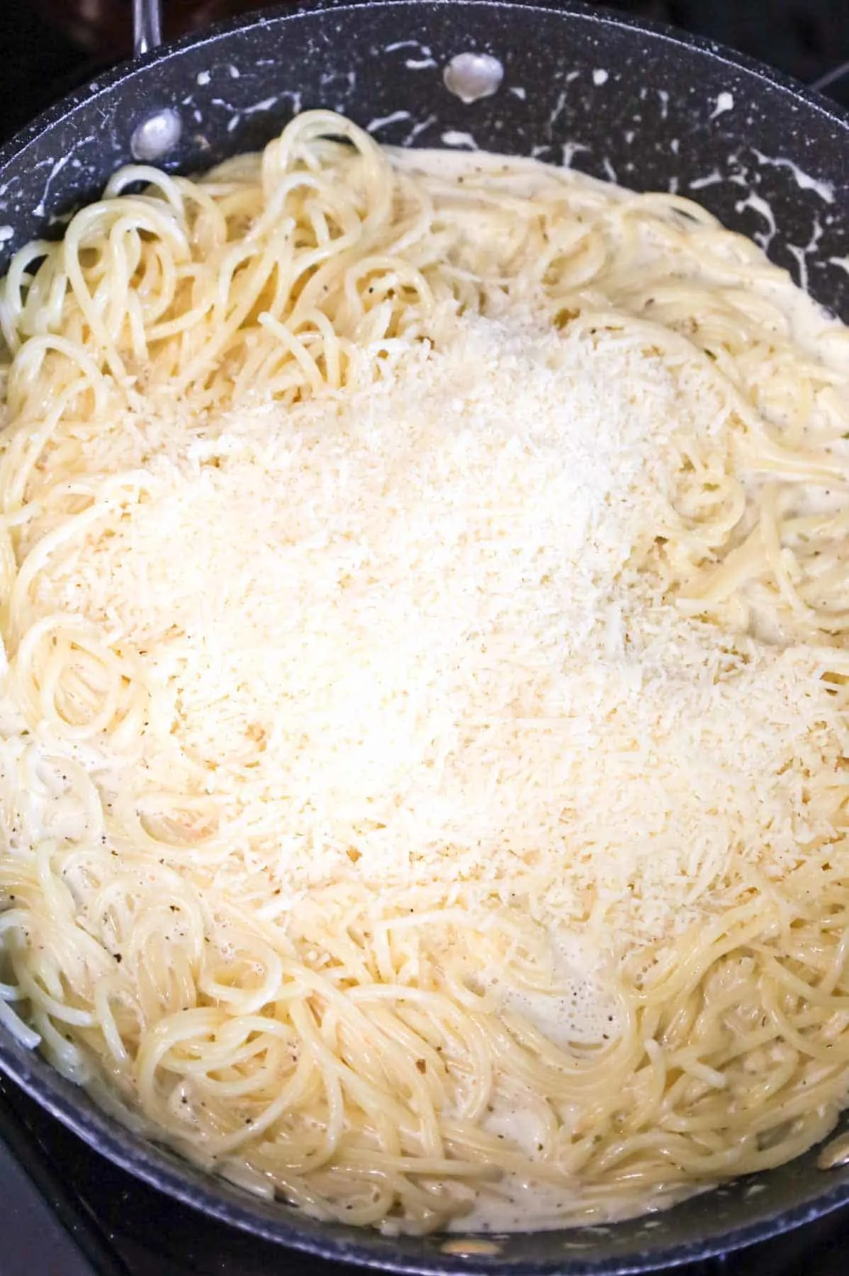 shredded parmesan cheese on top of creamy spaghetti in a skillet