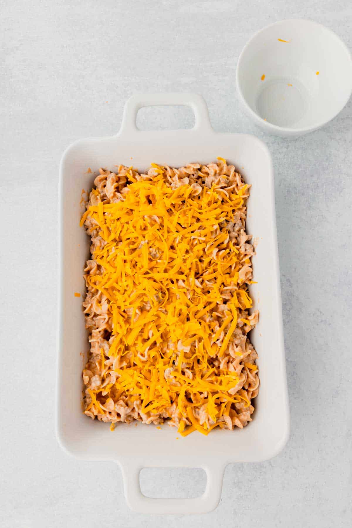 shredded cheddar cheese on top of beef noodle mixture in a casserole dish