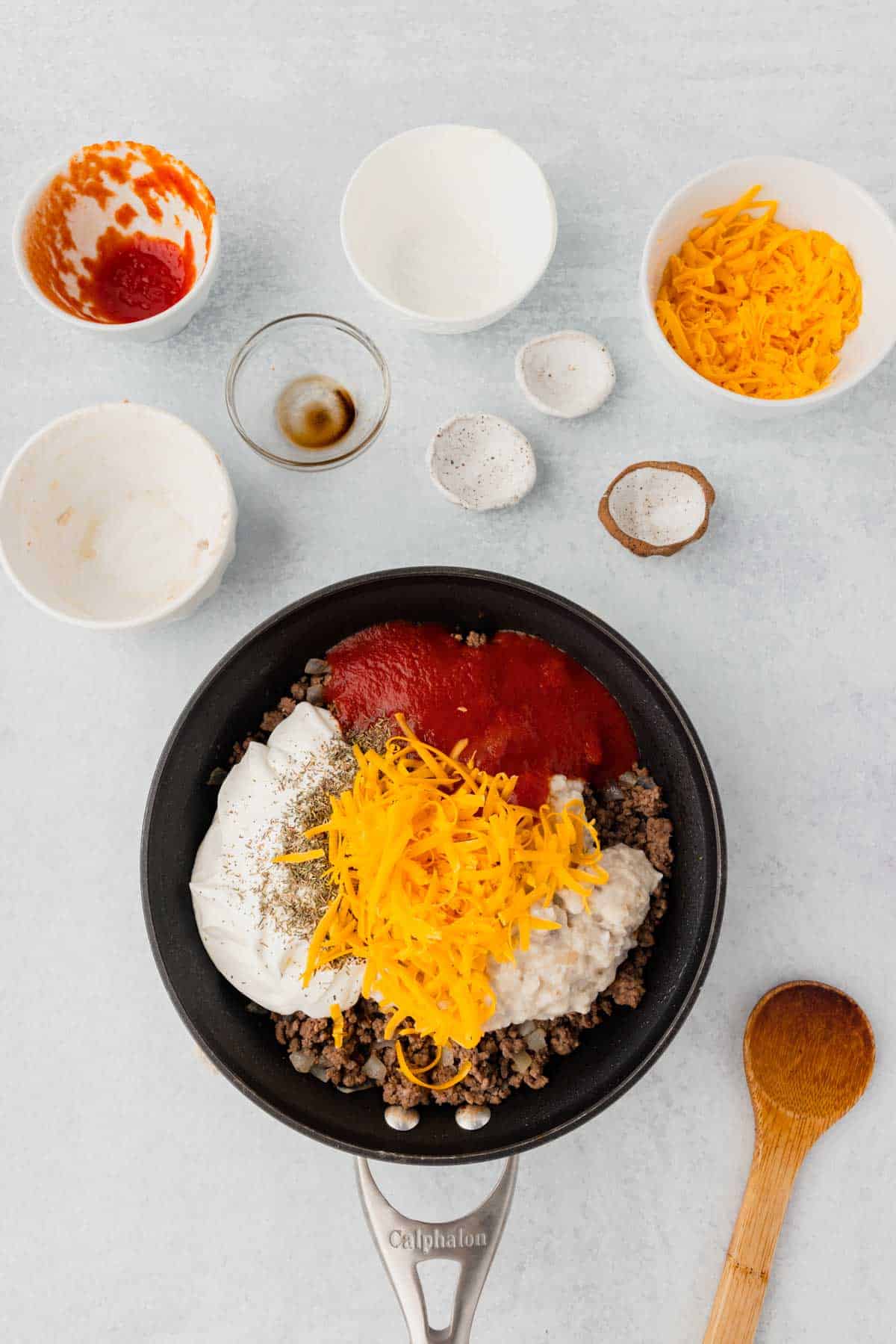 shredded cheddar cheese, spices, tomato sauce, cream of mushroom soup and sour cream on top of cooked ground beef in a skillet