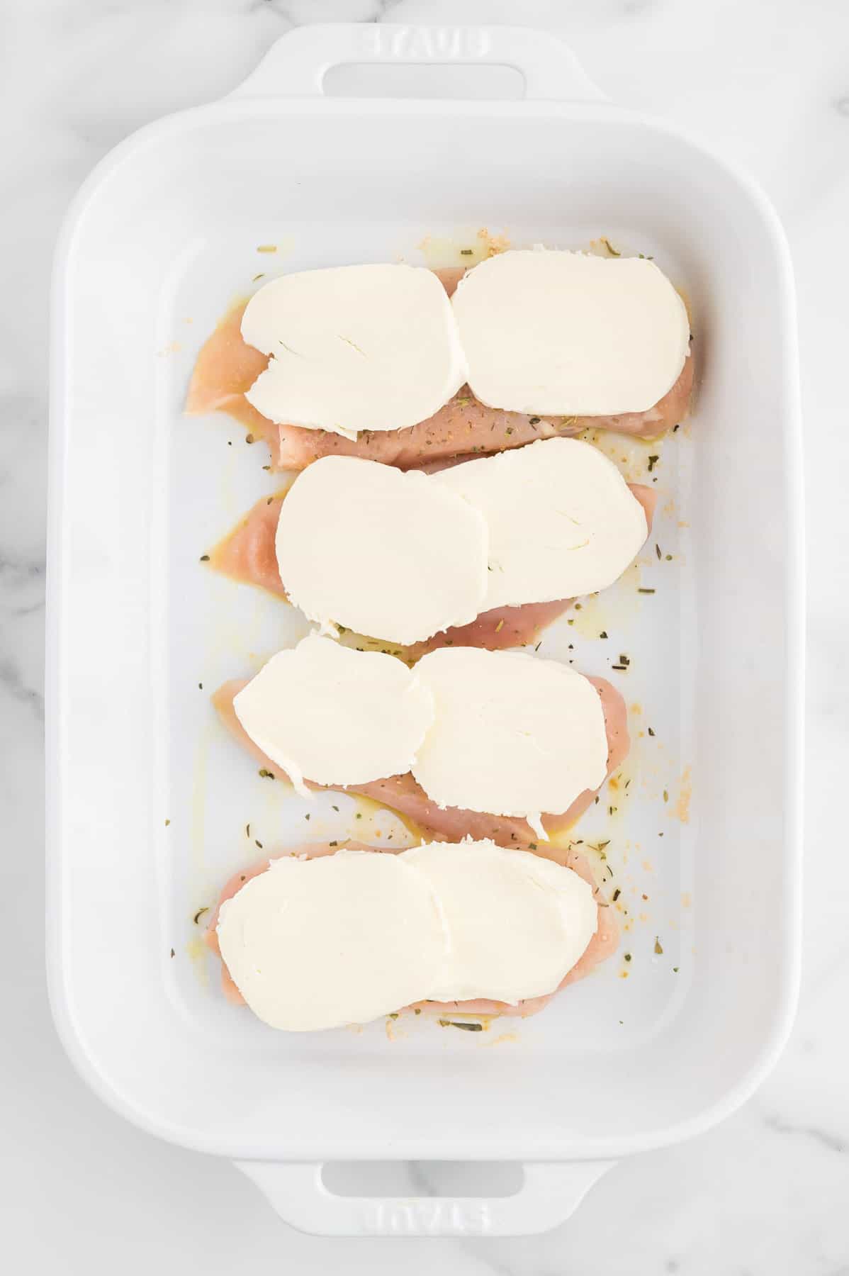 fresh slices of mozzarella on top of chicken breasts in a baking dish