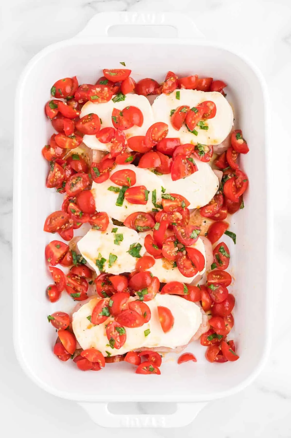 cherry tomato bruschetta mixture over mozzarella and chicken breasts in a baking dish