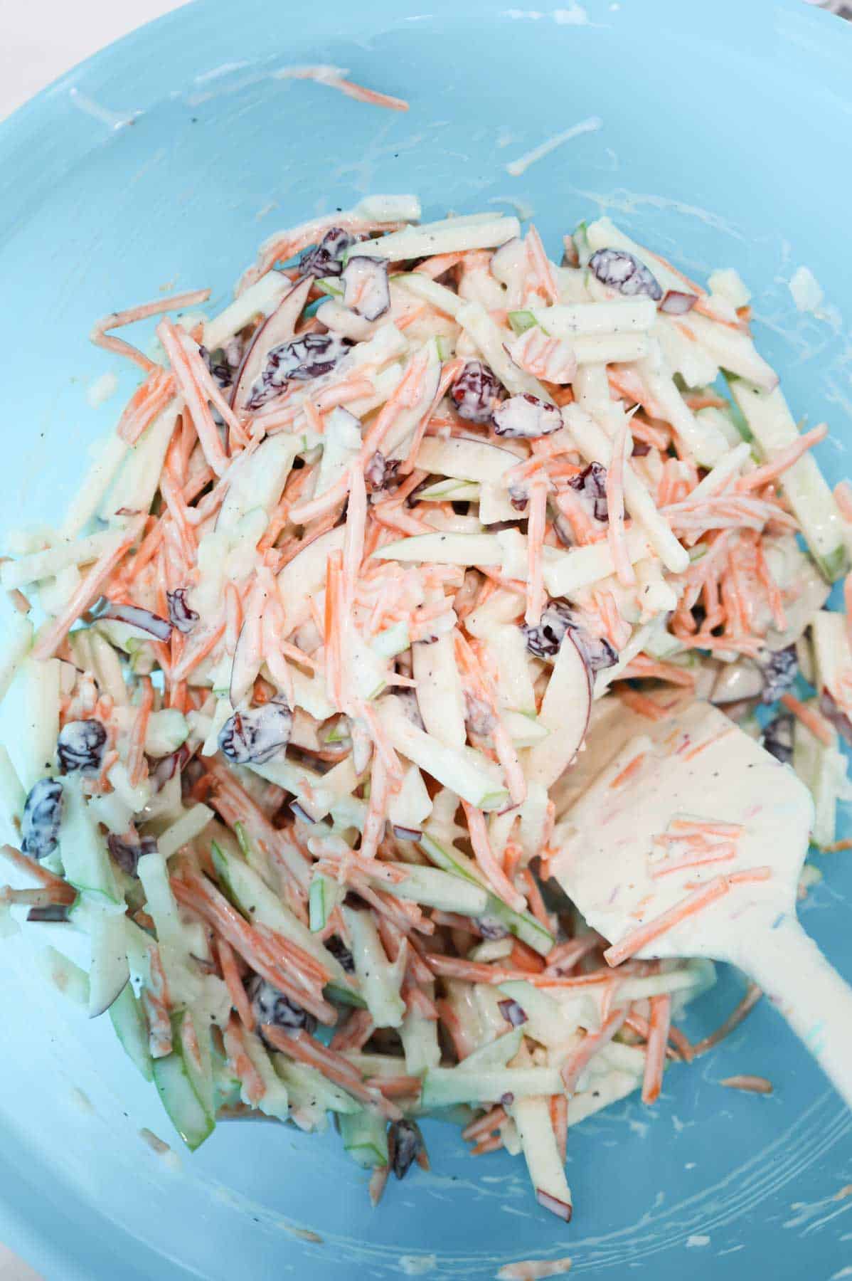 carrot apple salad ingredients being stirred with dressing