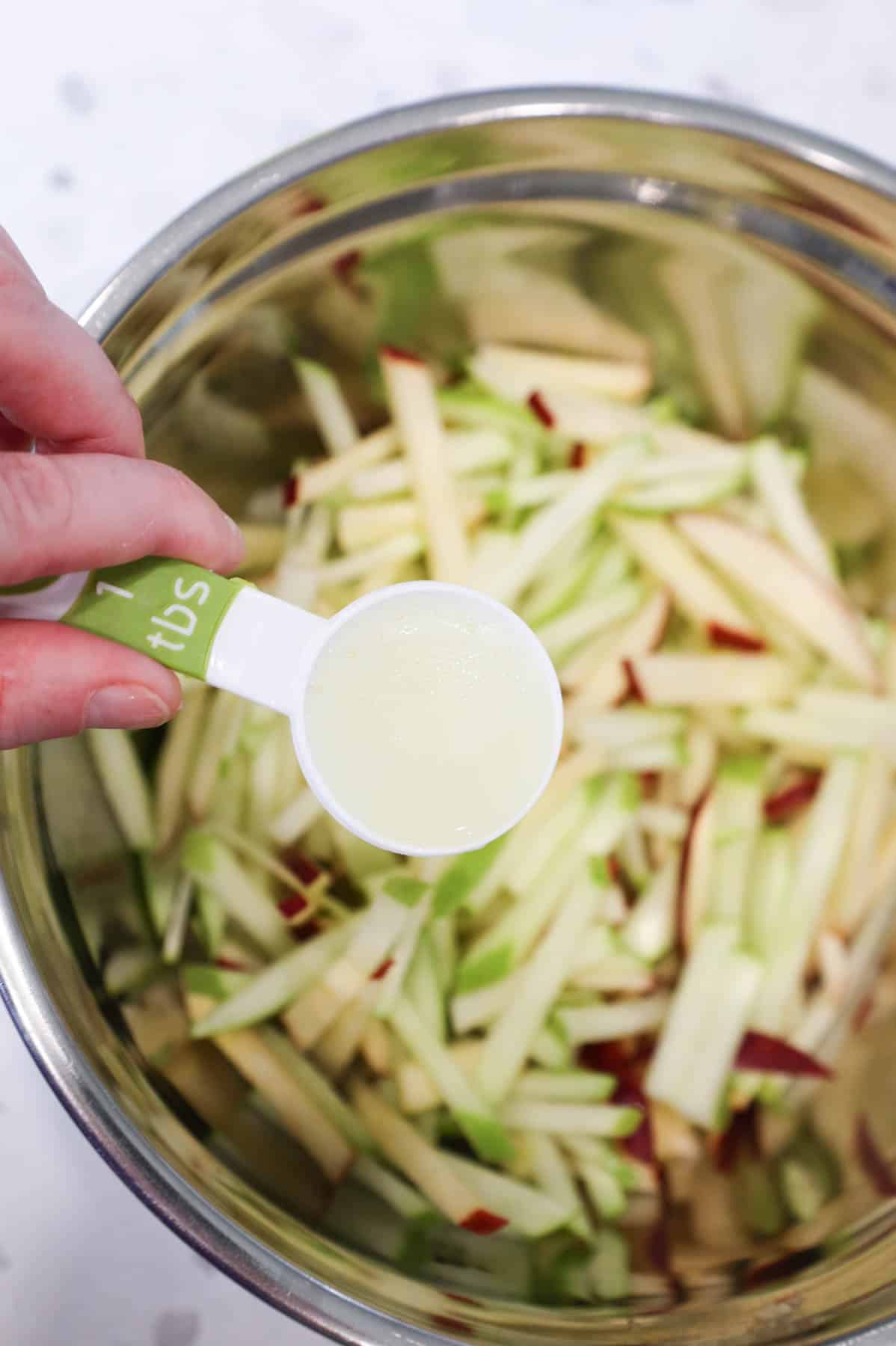 lemon juice being poured over matchstick apples in a bowl