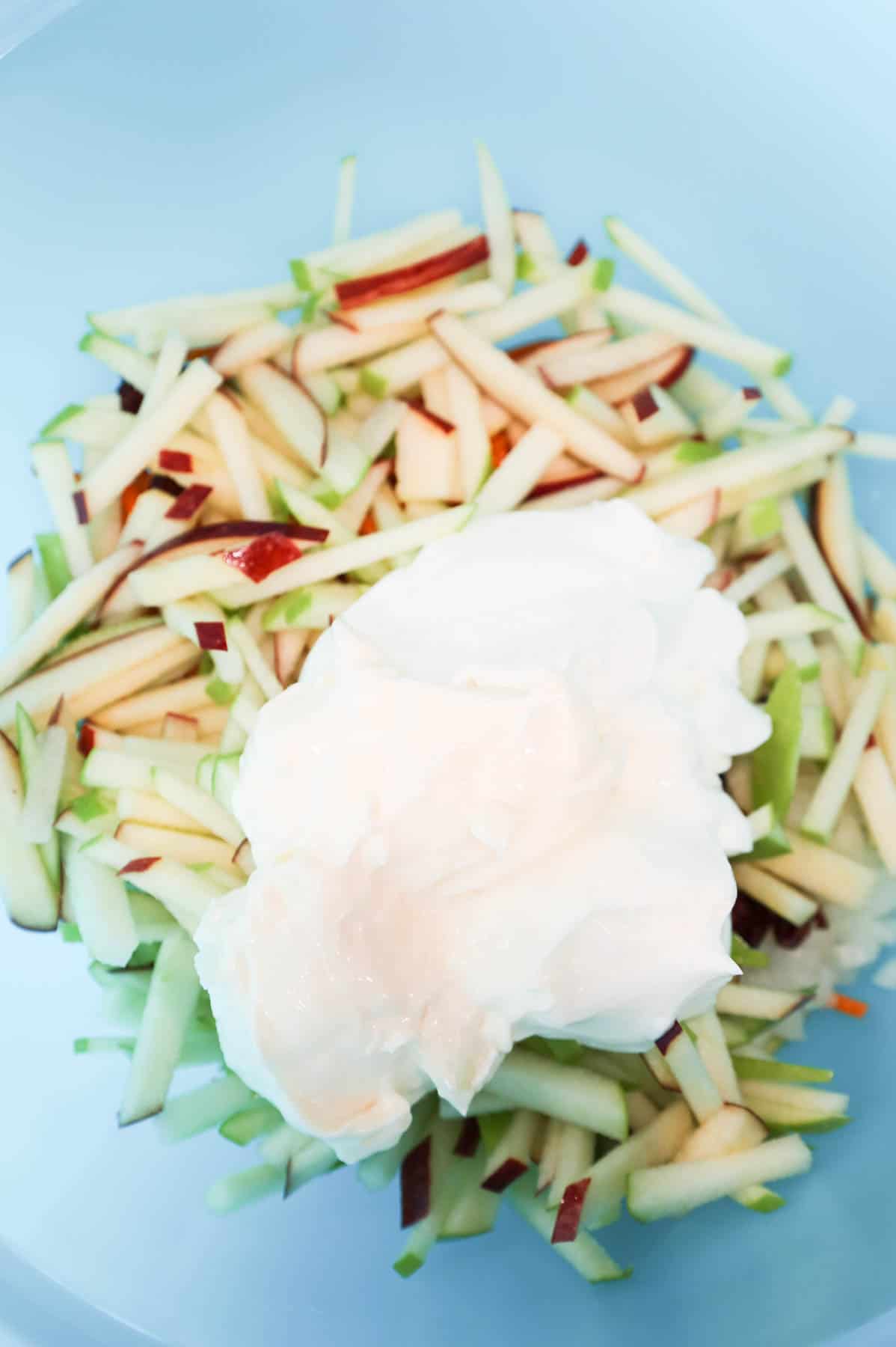 vanilla yogurt and mayo on top of carrot apple salad ingredients in a mixing bowl