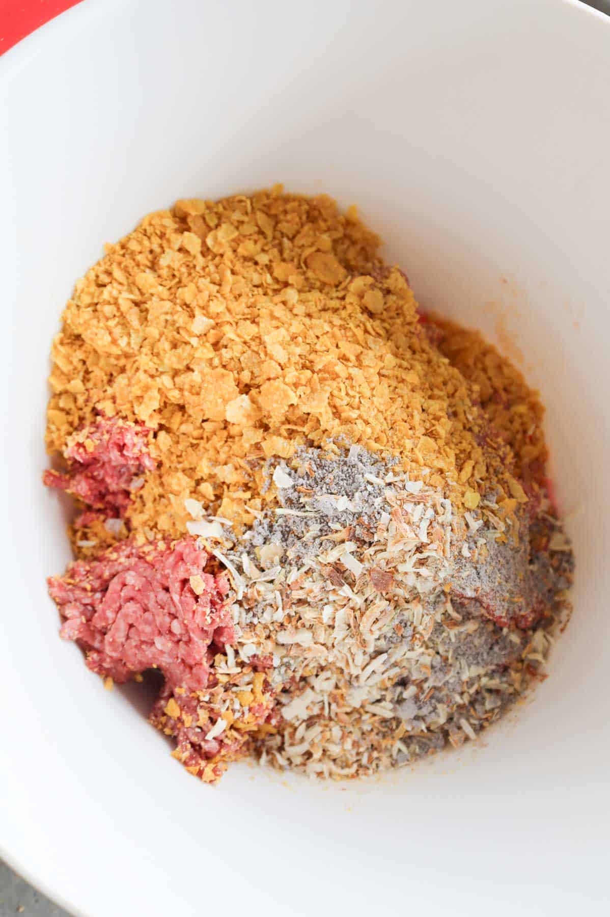 crushed cornflakes, onion soup mix on top of ground beef in a mixing bowl