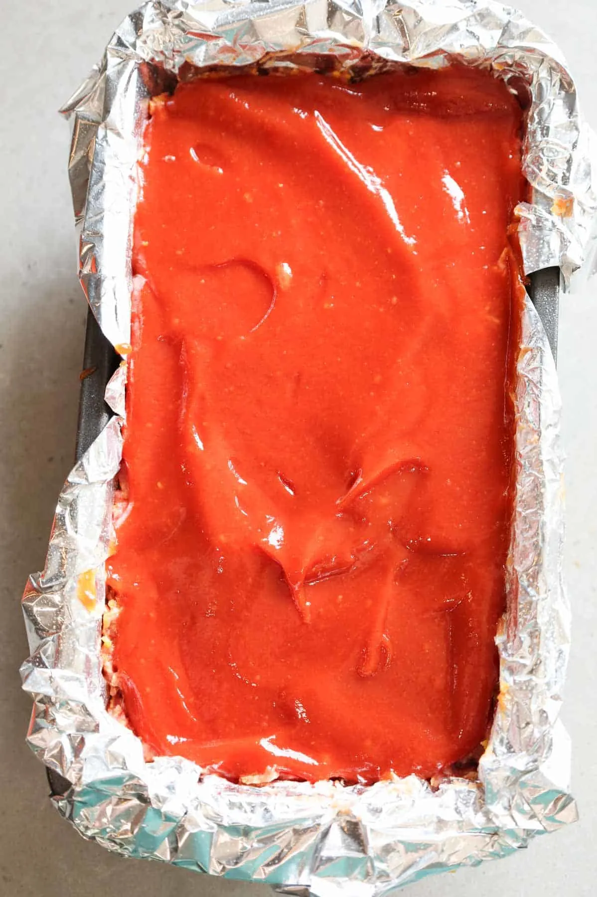 ketchup glaze spread on top of meatloaf in a loaf pan
