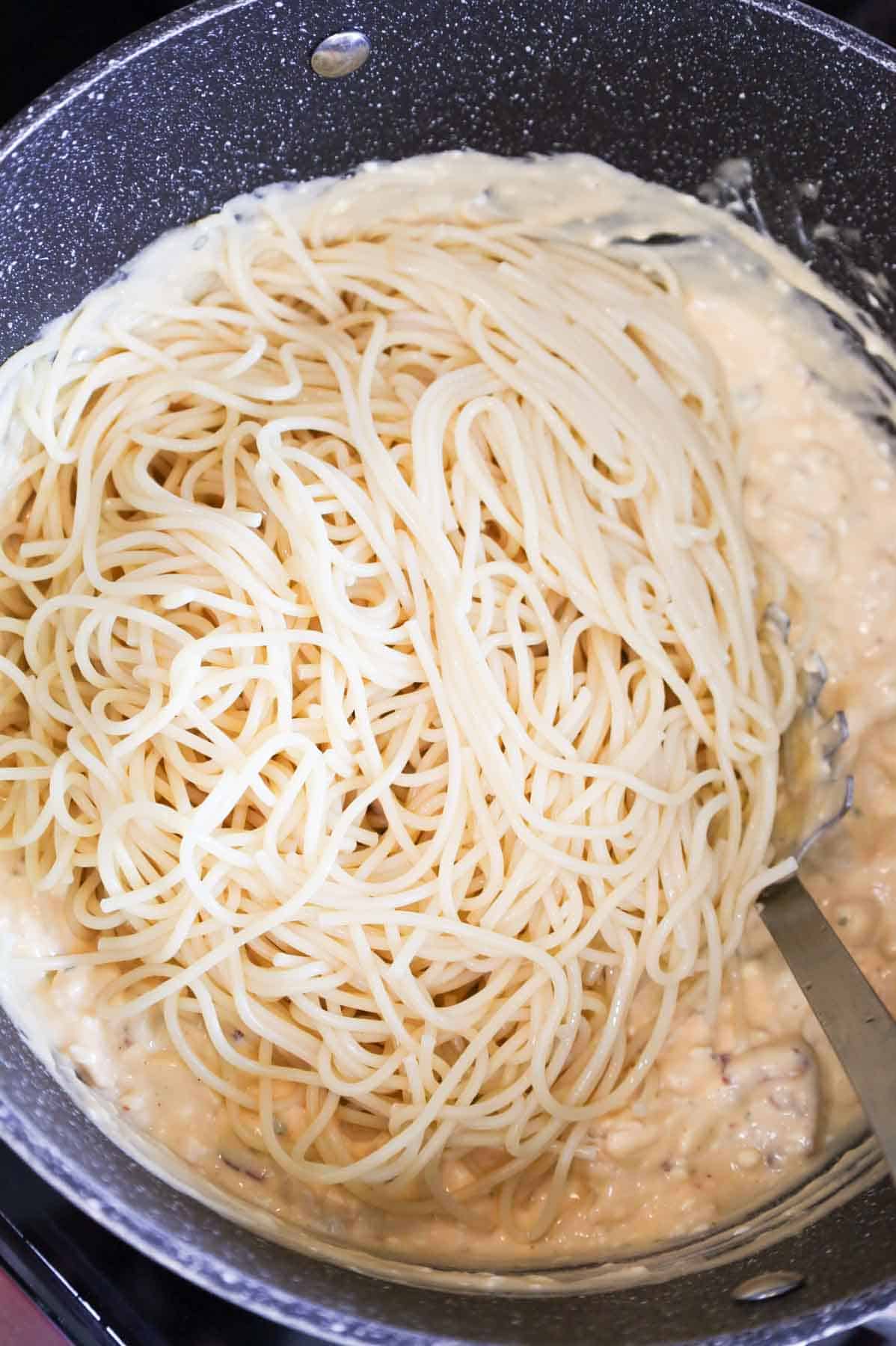 cooked spaghetti added to pot with creamy chicken sauce