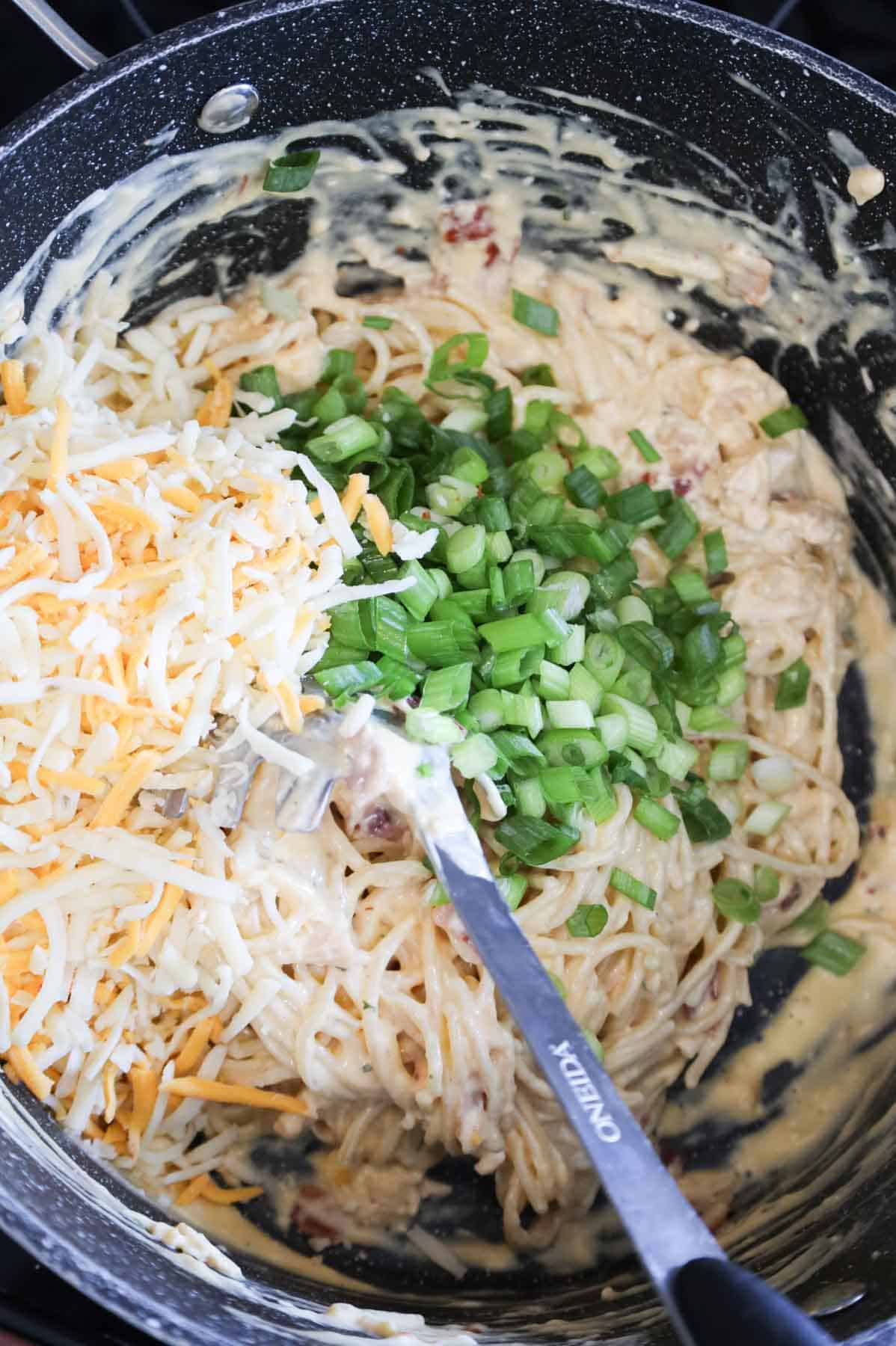 shredded cheese and chopped green onions on top of creamy chicken spaghetti in a pot