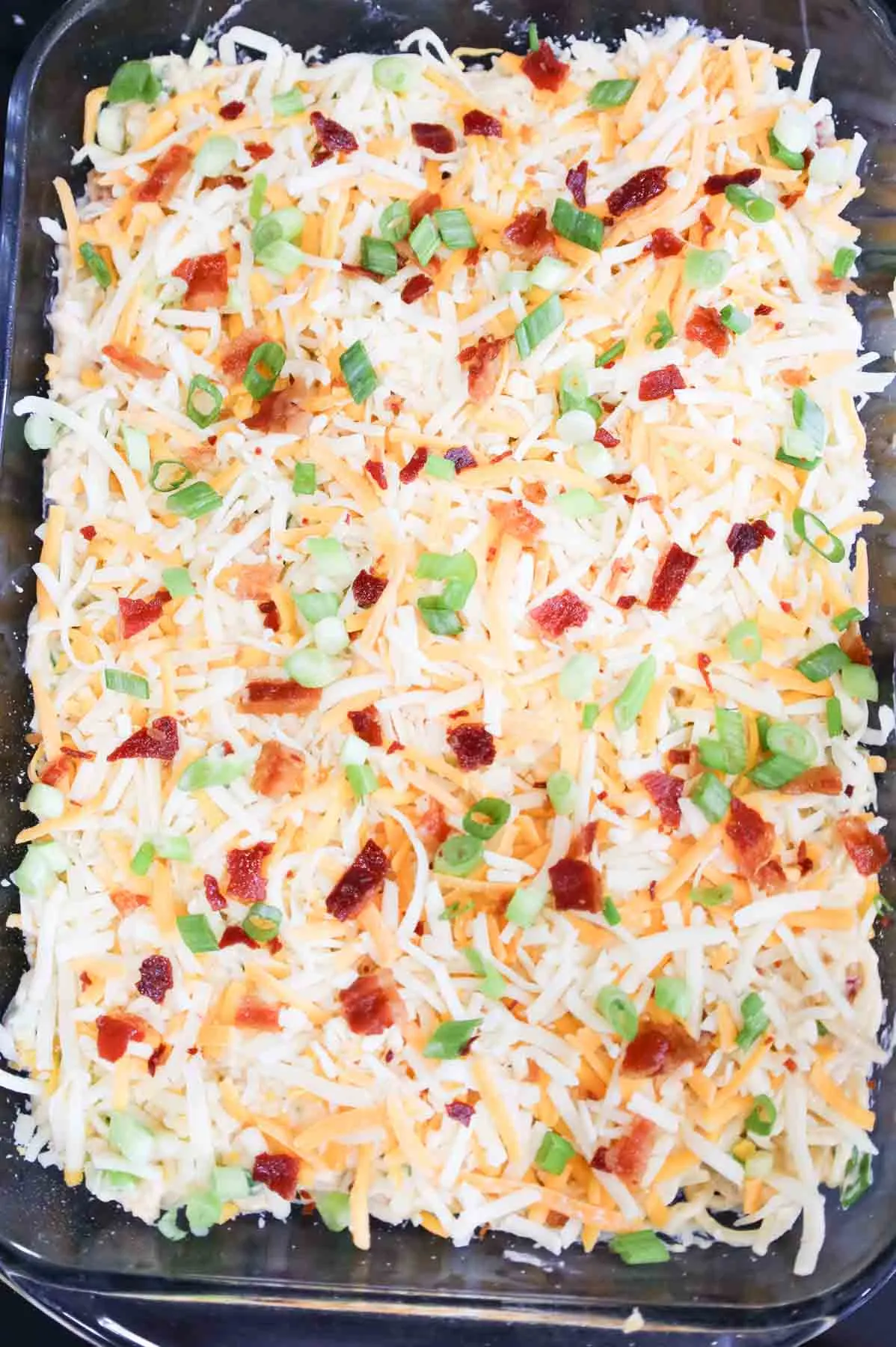 shredded cheese, green onions and bacon on top of chicken spaghetti in a baking dish