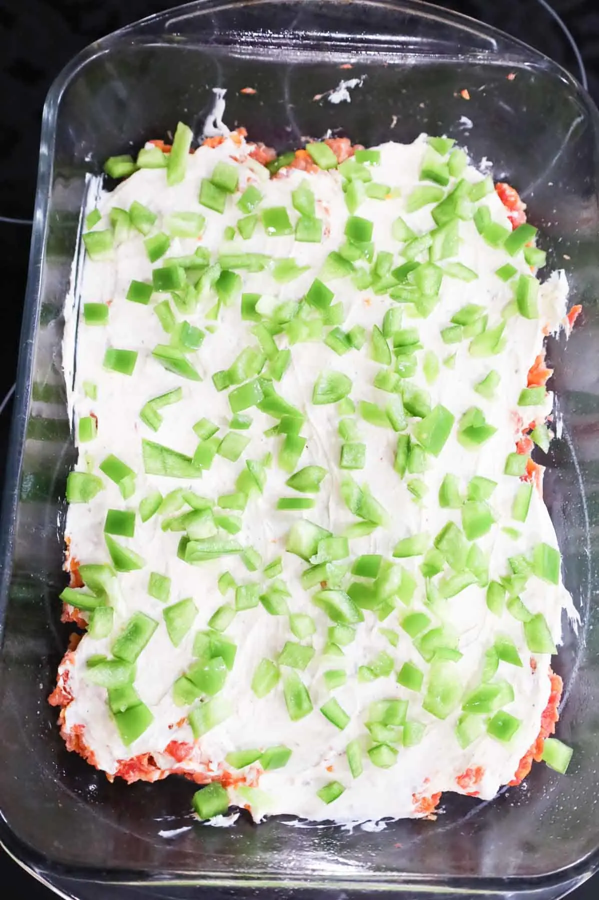 diced green bell peppers on top of cream cheese and meatloaf mixture in a baking dish
