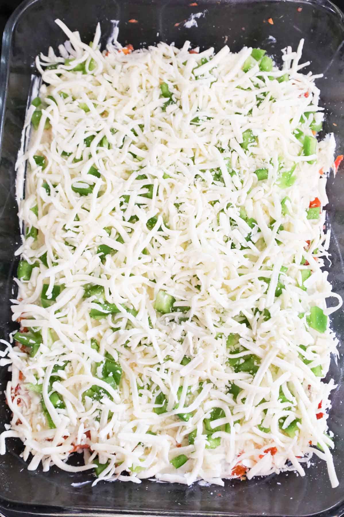 shredded mozzarella and green peppers on top of meatloaf mixture in a baking dish
