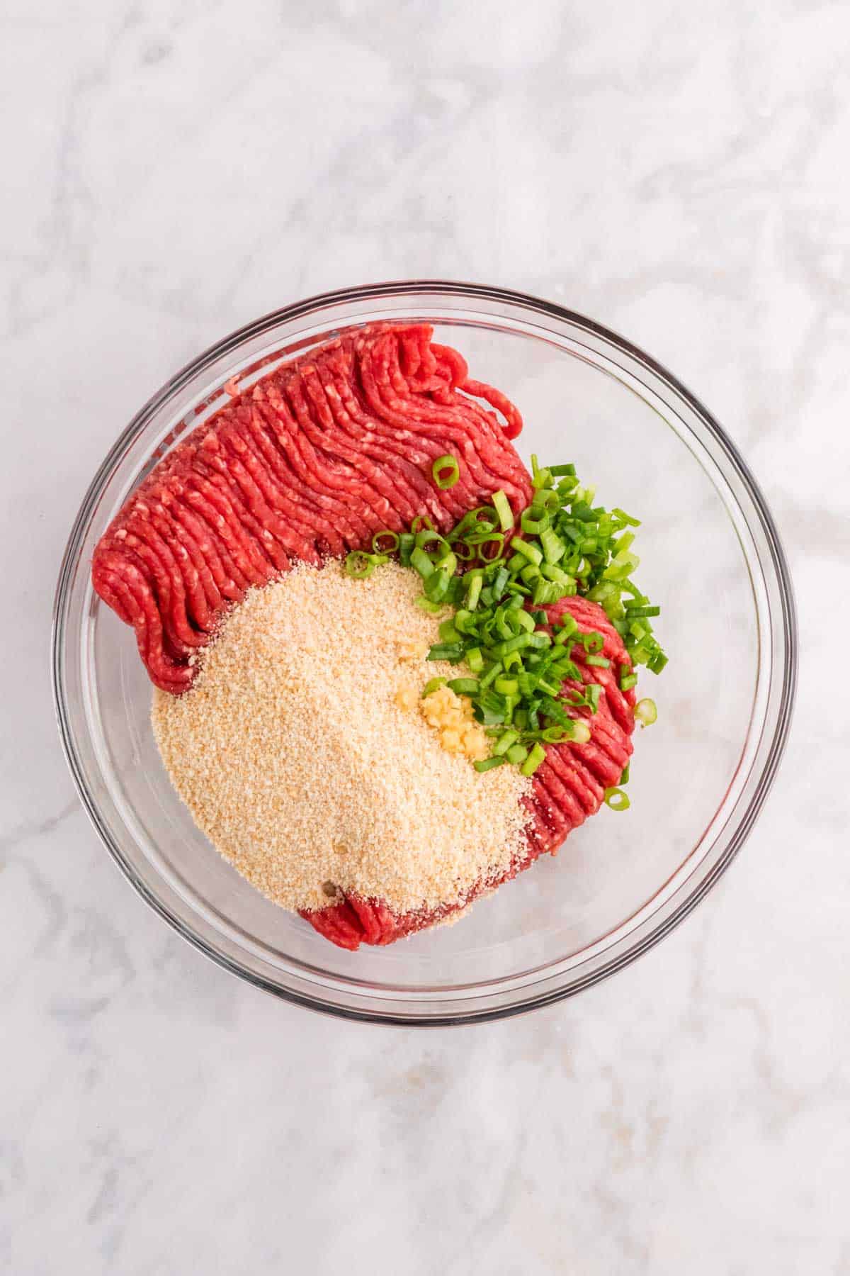raw ground beef, bread crumbs, minced garlic and chopped green onions in a bowl