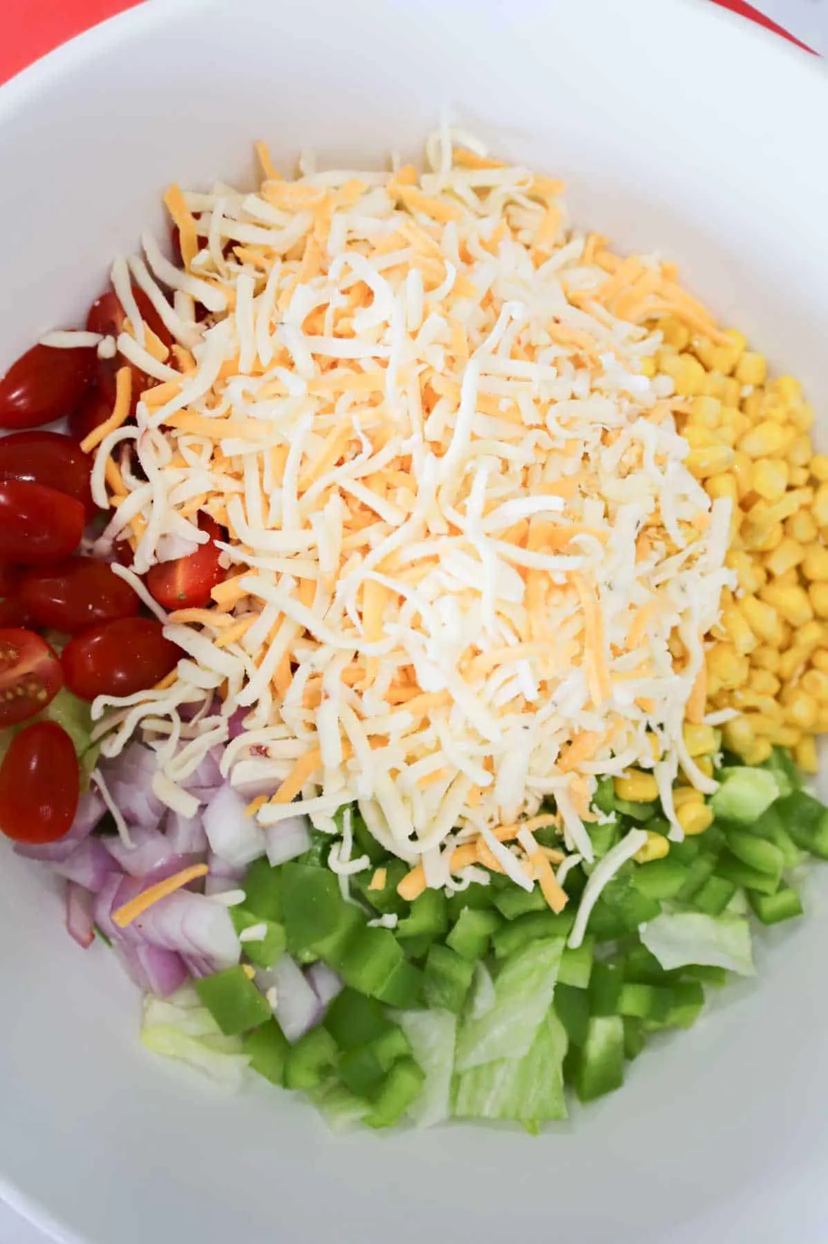 shredded cheese, tomatoes, peppers, onions and corn on top of lettuce in a bowl